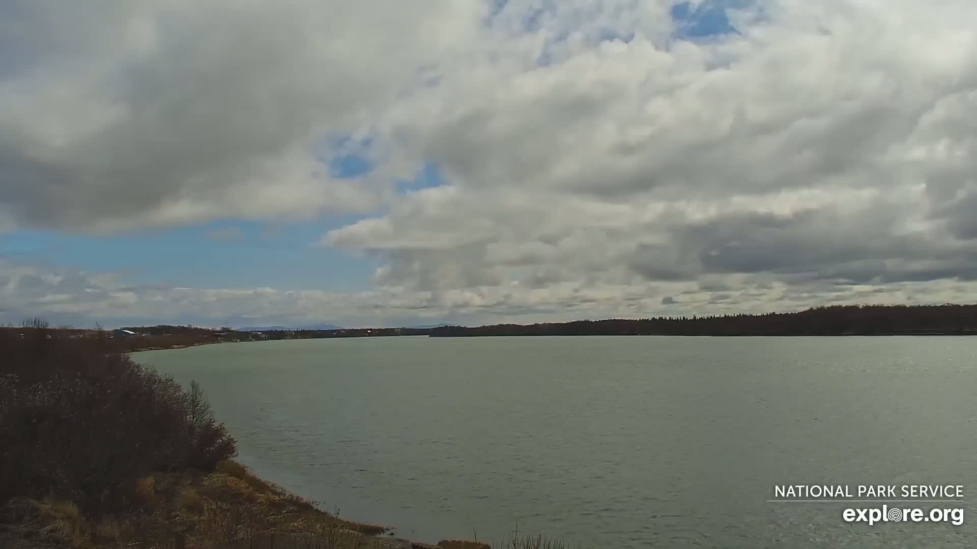 A wide, calm body of water stretches to a treeline under a partly cloudy sky.