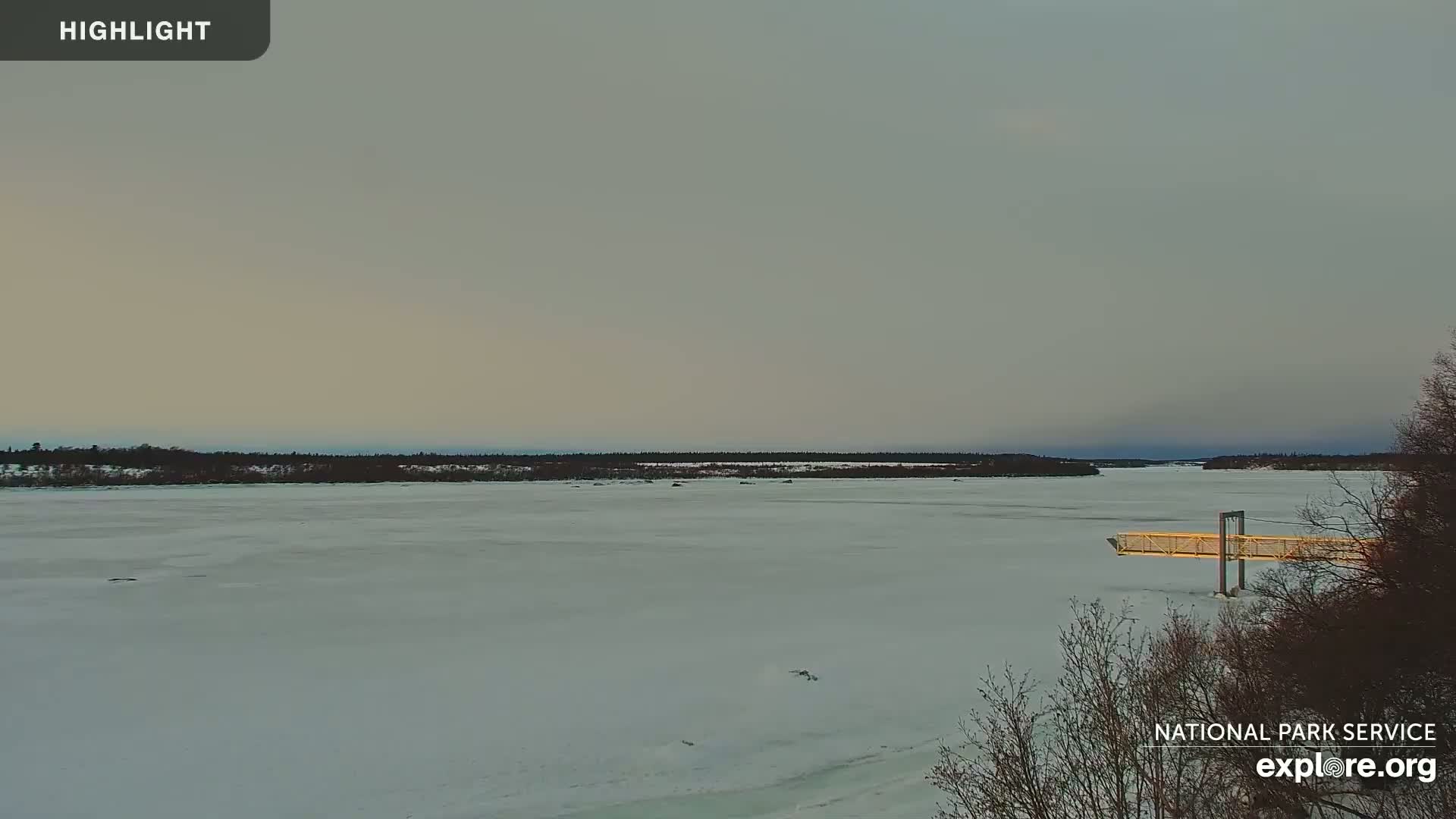 A wide, frozen river stretches to a treeline under a pale, overcast sky.