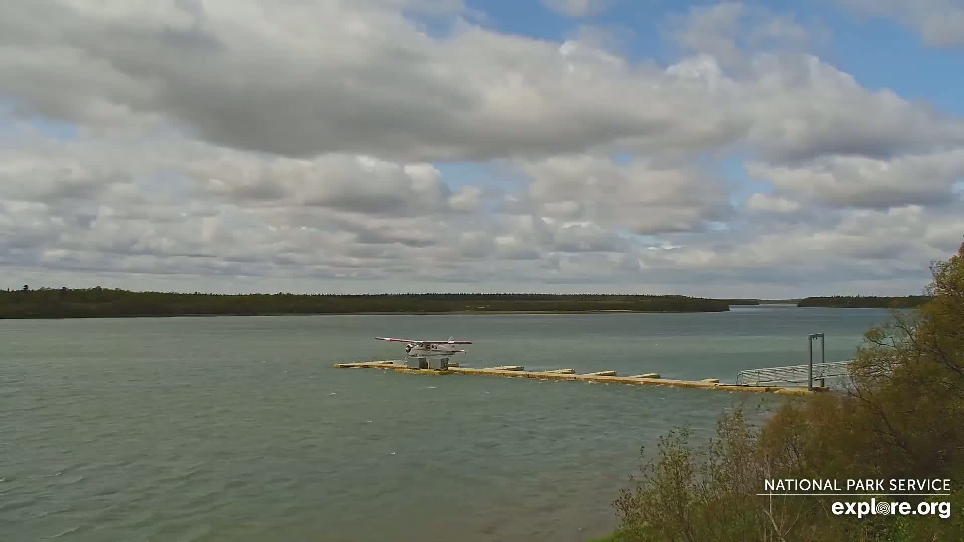 A seaplane sits on a dock in a calm body of water under a partly cloudy sky.