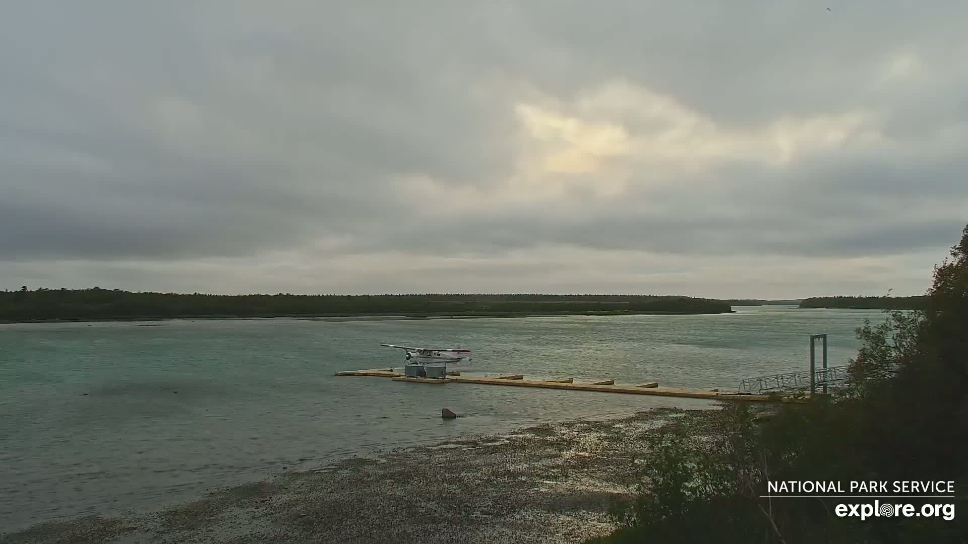 A seaplane sits on a dock in a calm body of water under an overcast sky.