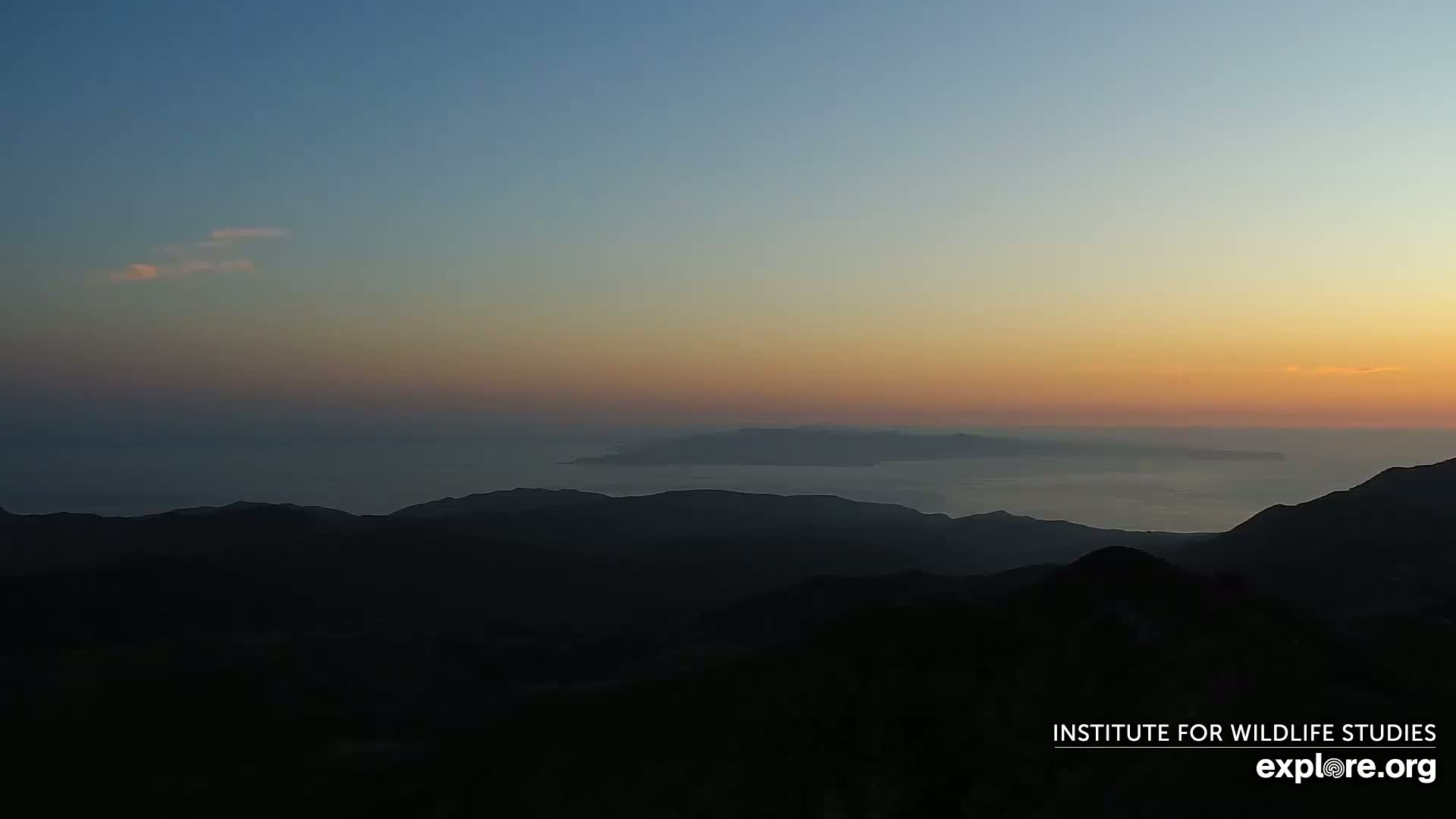 A hazy sunset illuminates distant islands and a mountainous landscape.