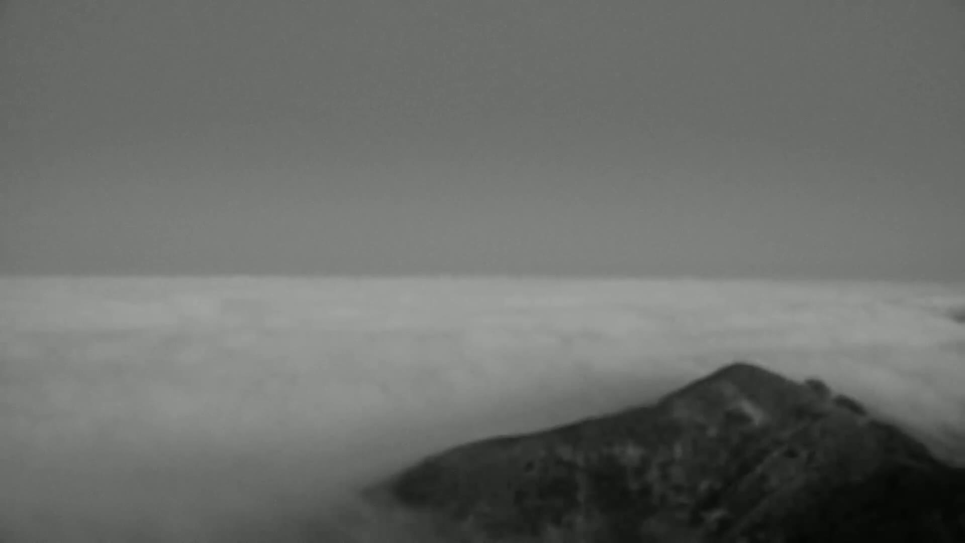 A dark, rocky hilltop is partially visible above a thick layer of fog under a gray sky.