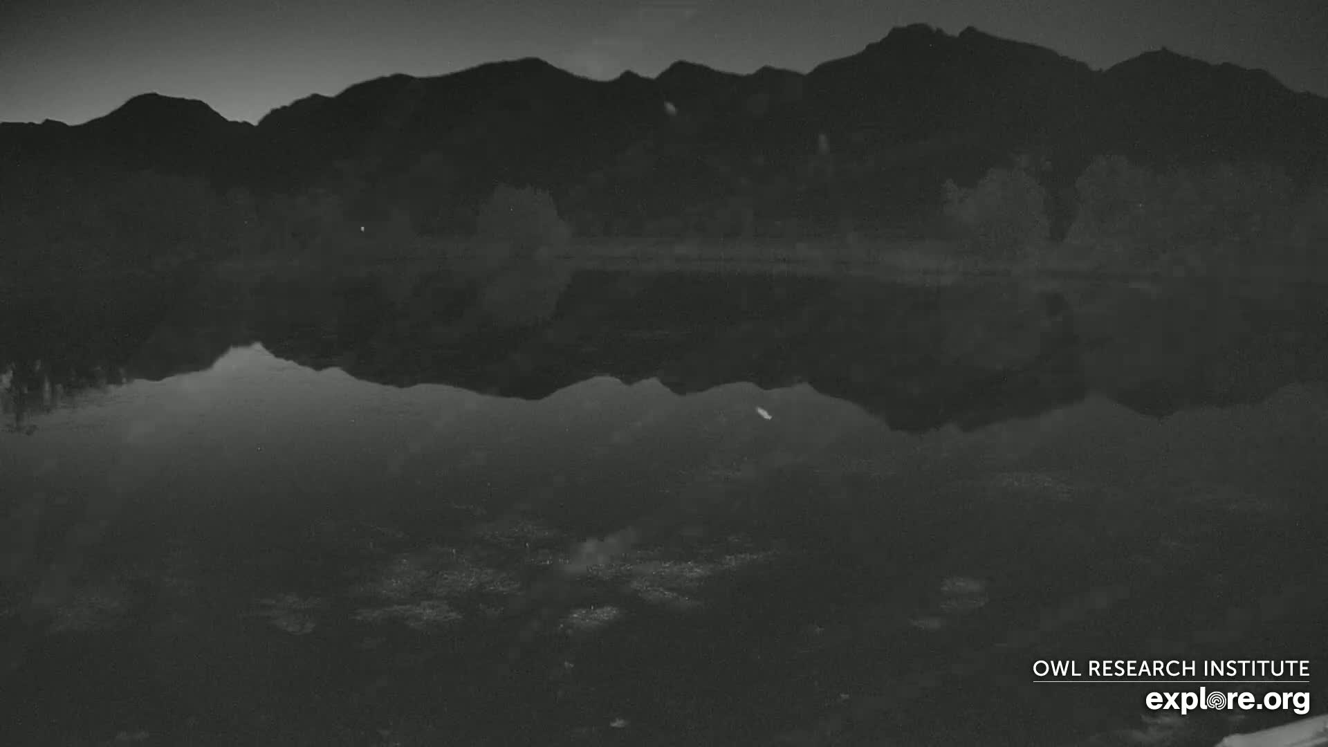 A dark body of water reflects a silhouetted mountain range under a night sky.