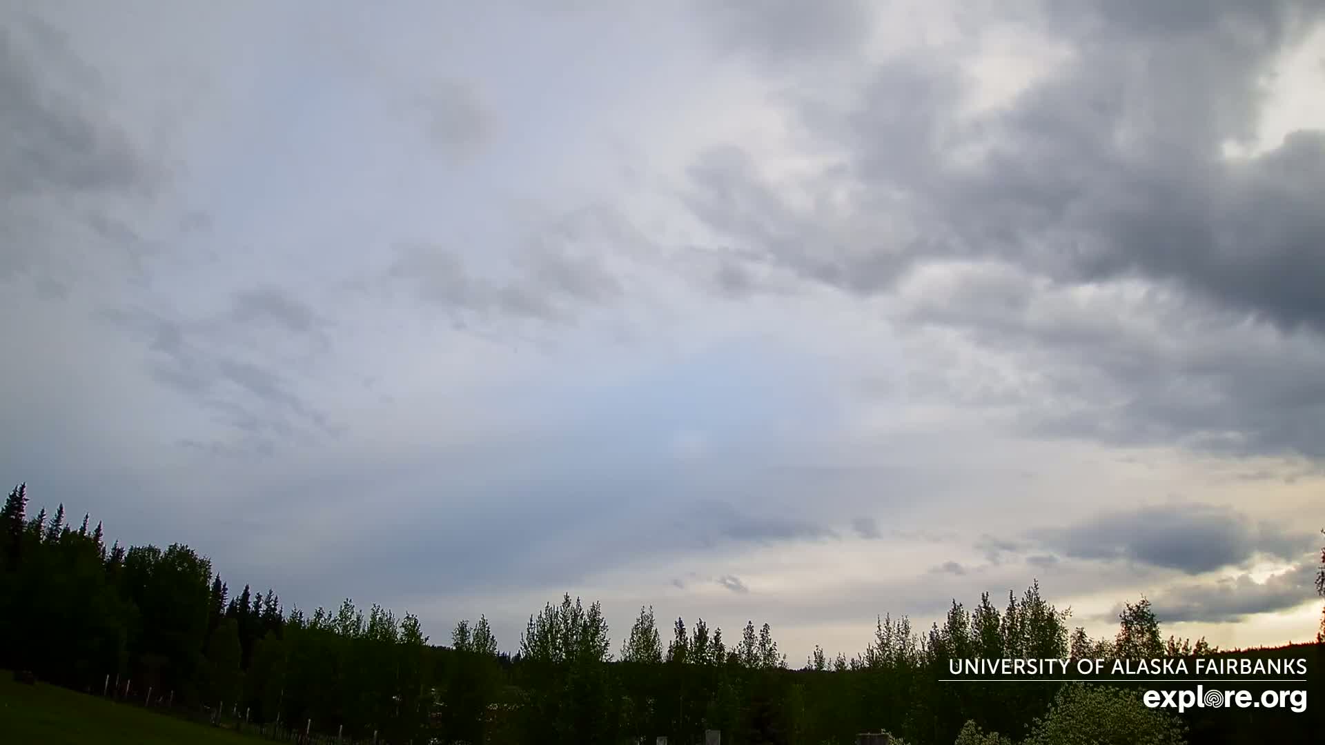 A mostly cloudy sky with a line of dark trees in the foreground.