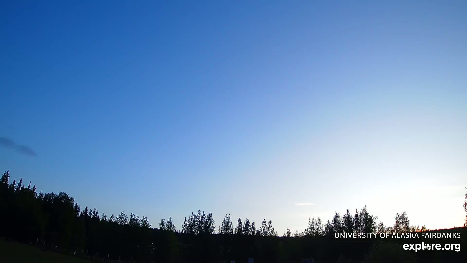 Under a clear, twilight sky, a line of dark silhouetted trees stretches across the bottom of the image.