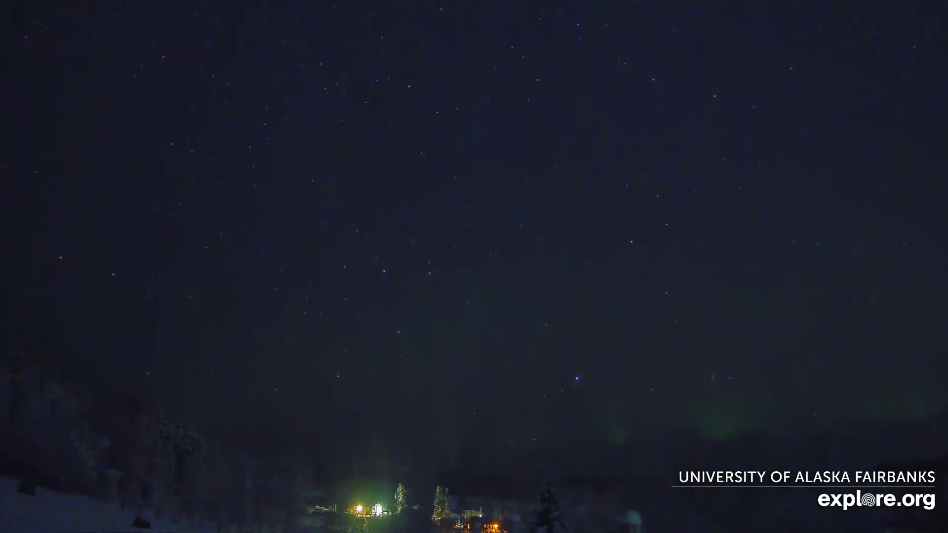 A mostly cloudy sky, with some brighter areas, hangs over a dark line of trees.