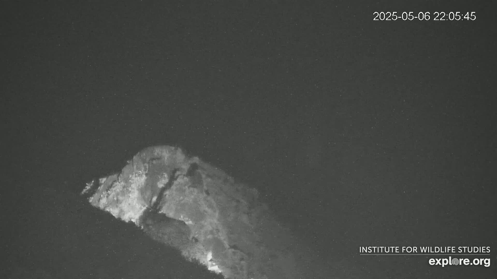 A nighttime, low-light image shows a rocky hillside, possibly volcanic, with faint light emanating from its base.