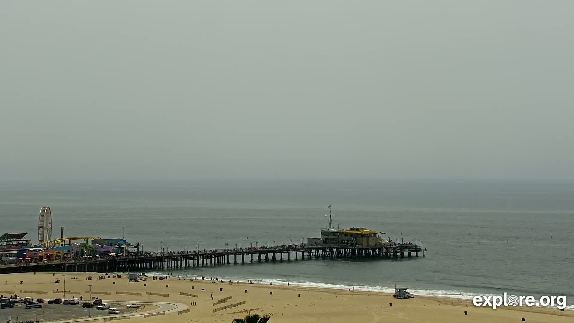 A long pier extends into a hazy, gray ocean, with a beach and amusement park features visible on the shore.