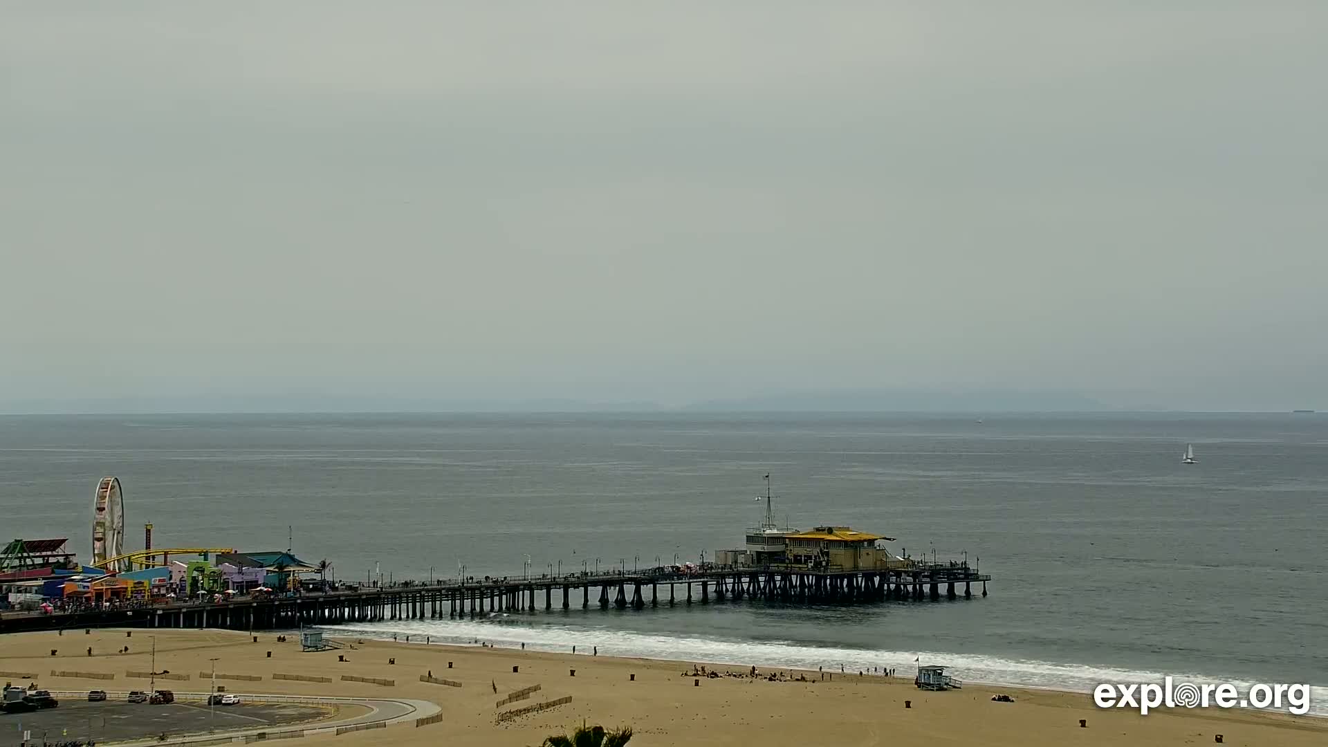 A long pier extends from a sandy beach into a calm, gray ocean under an overcast sky.