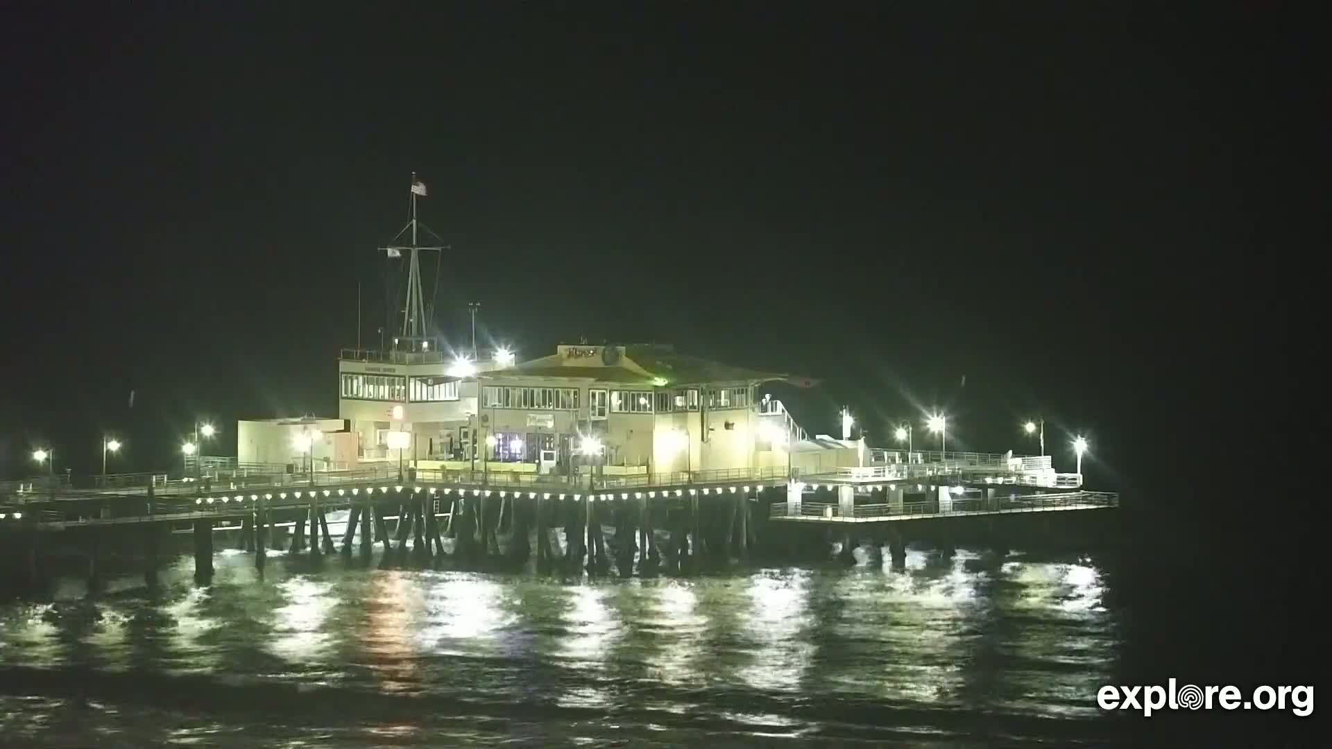 A brightly lit pier extends over dark, choppy water at night.