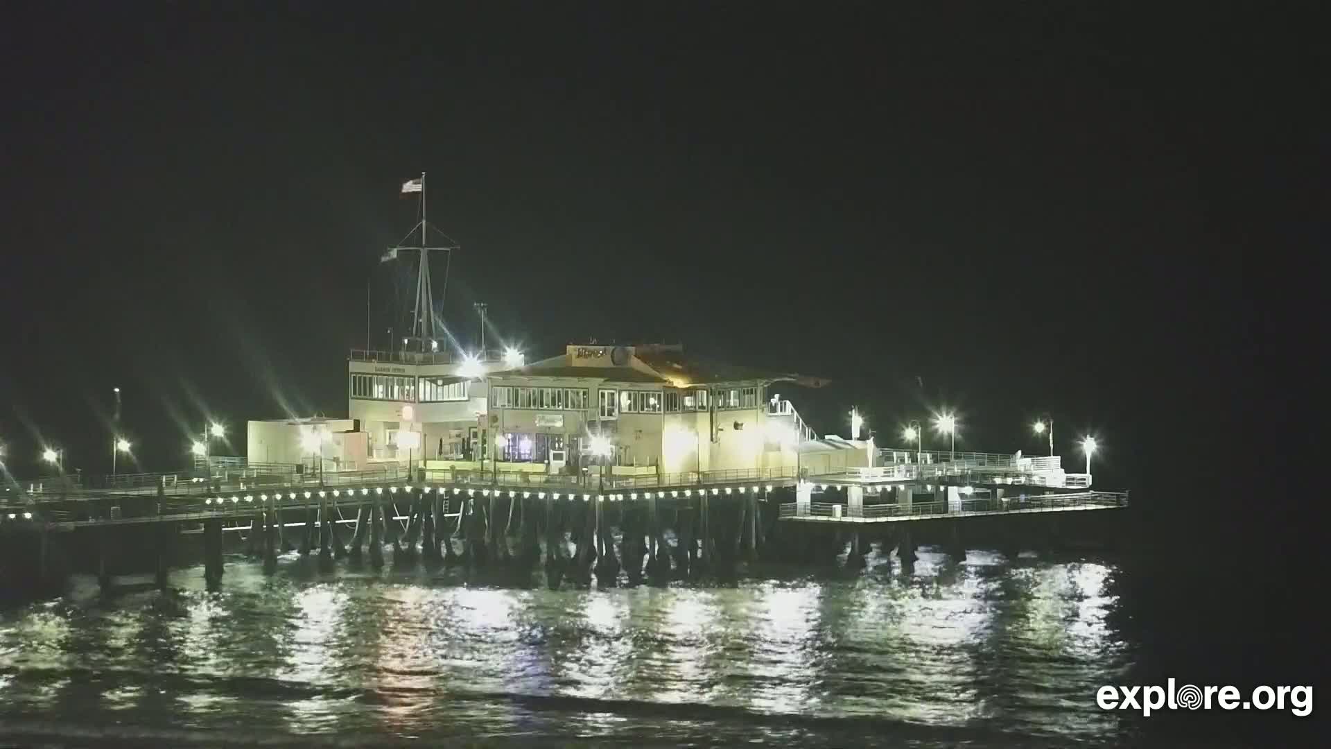 A brightly lit pier with a building on it sits on dark, wavy water under a night sky.