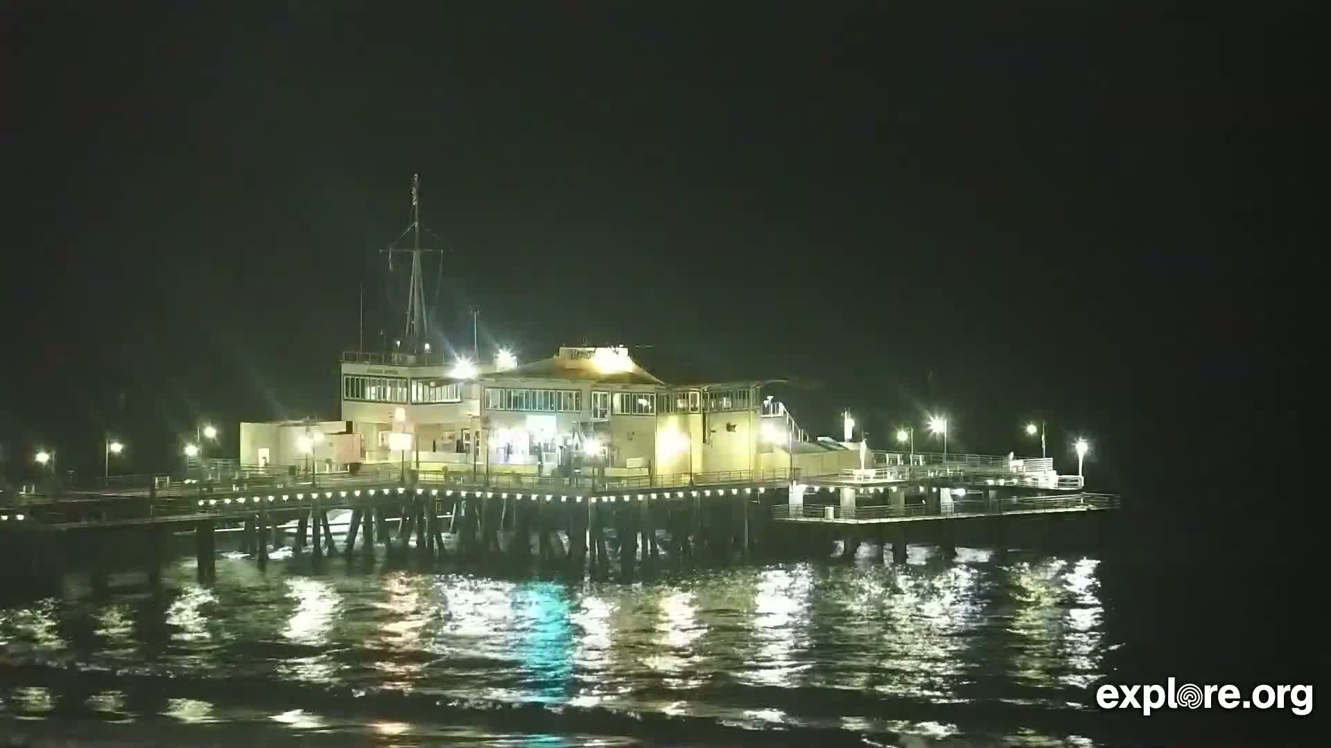 A brightly lit pier extends over dark, gently waving water at night.