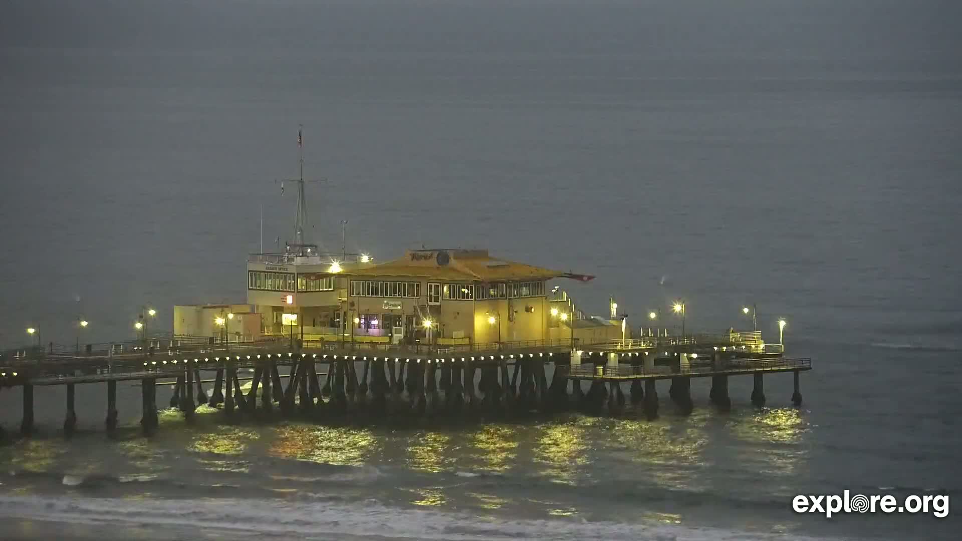 A pier with a building on it sits in slightly choppy water under a dark, overcast sky.