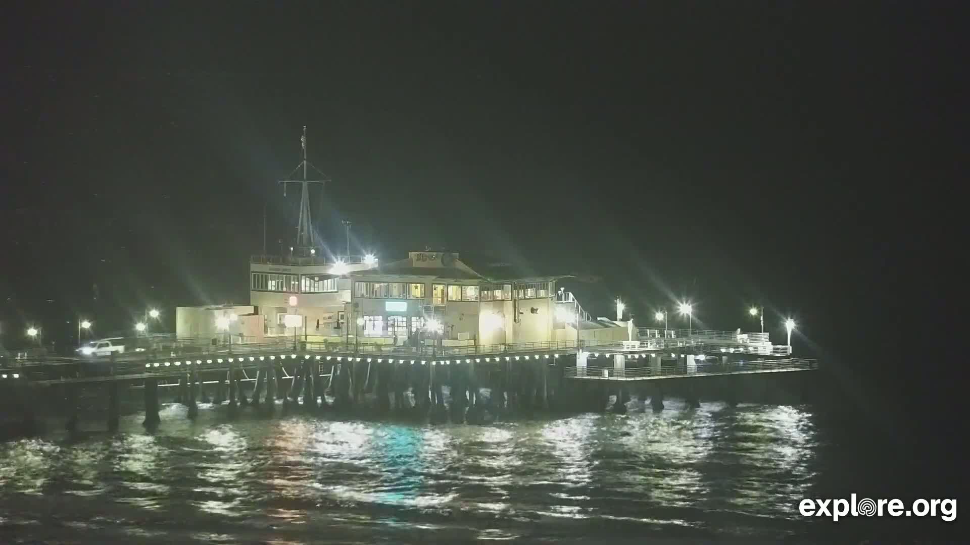 A brightly lit pier with a building on it sits on choppy water at night.
