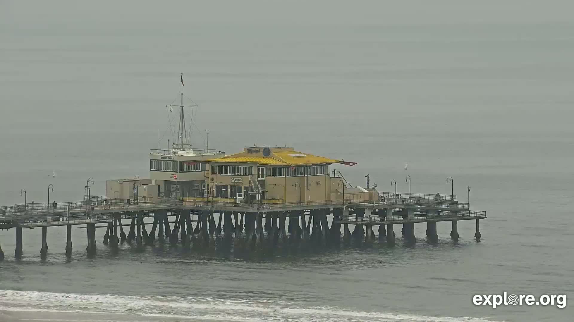 A pier with a building on it extends into a calm, gray ocean under an overcast sky.