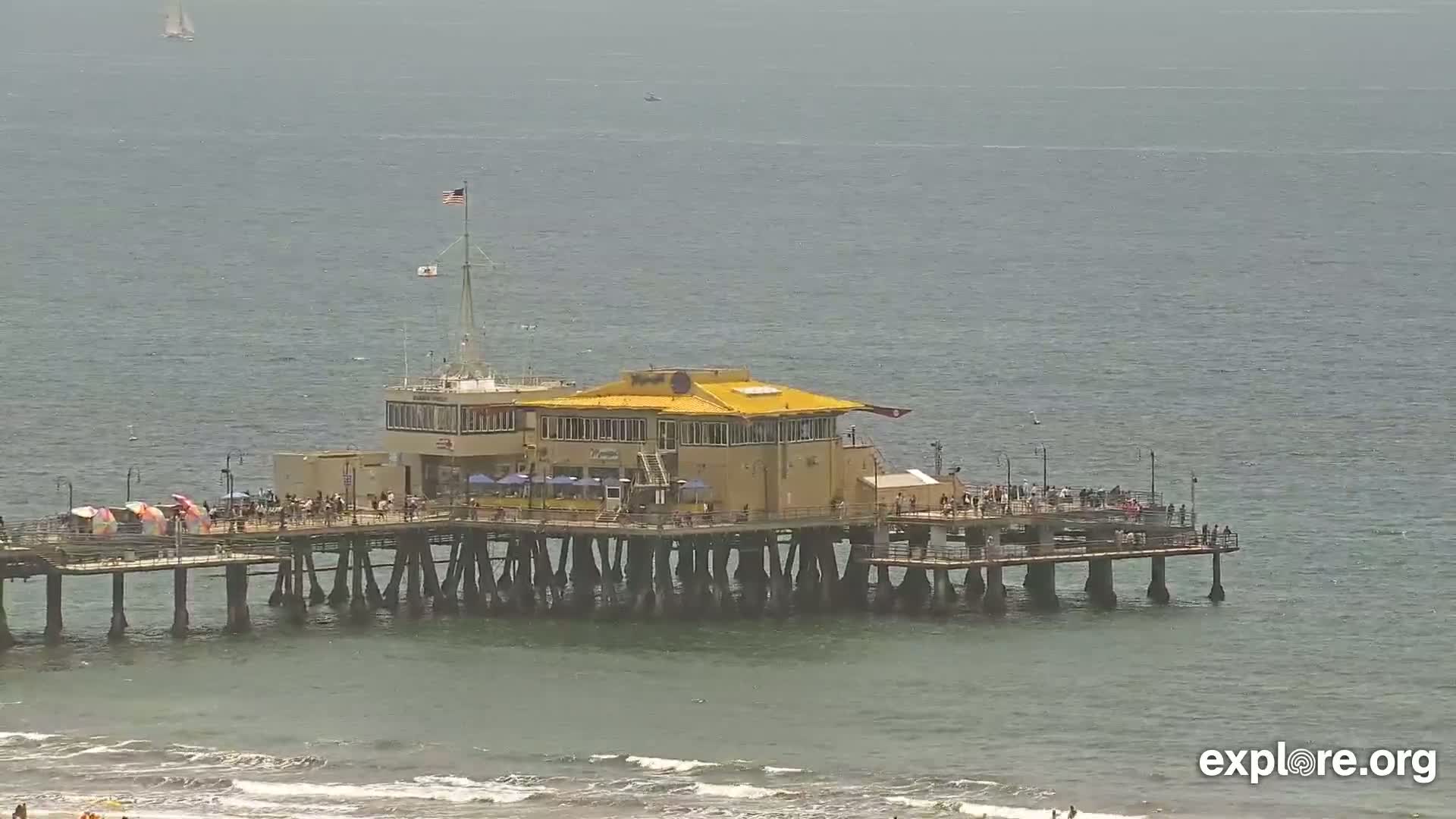 A pier with a building on it extends into a calm, gray ocean on a partly sunny day.