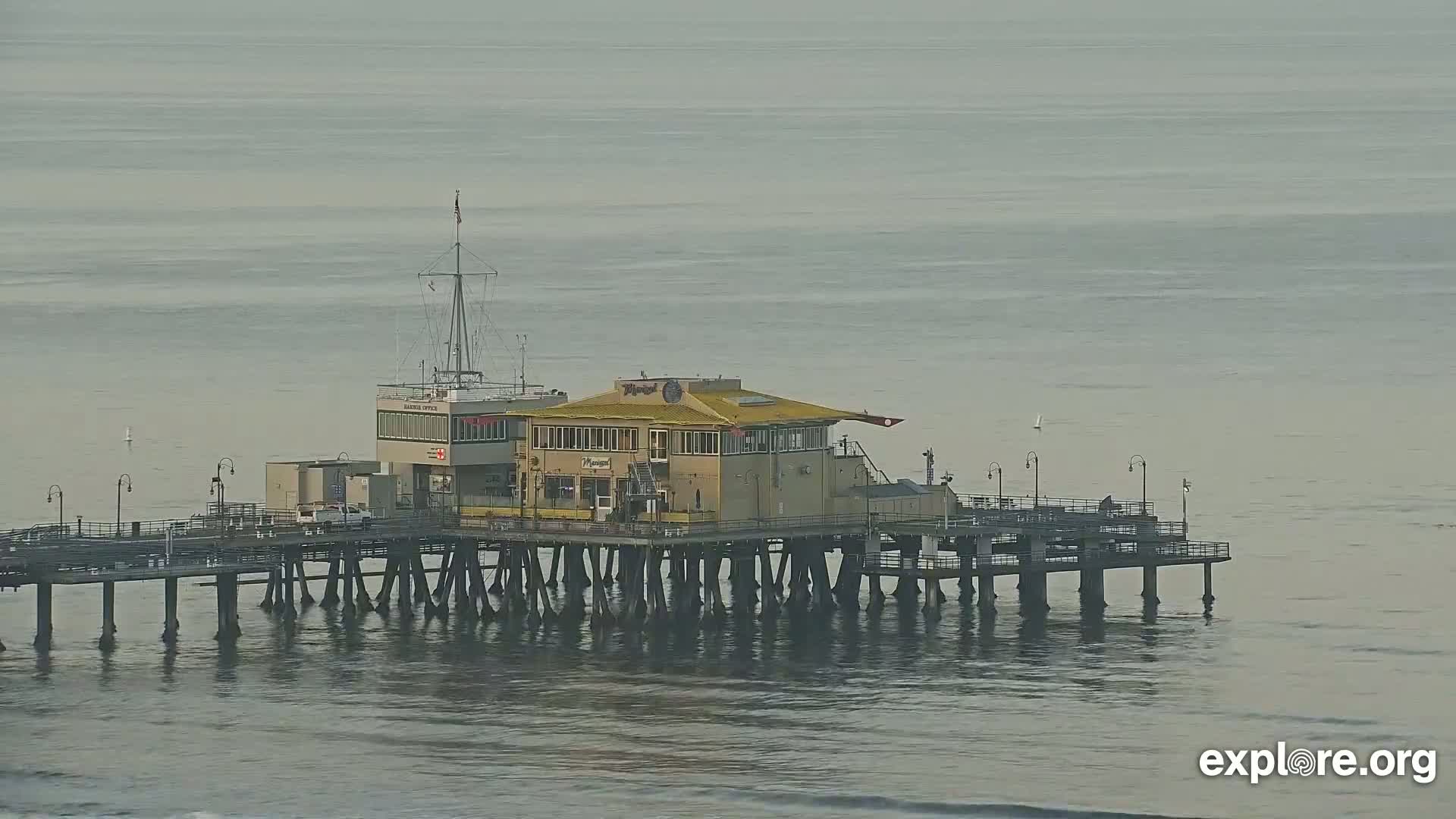 A pier with a building on it extends into a calm, gray ocean.