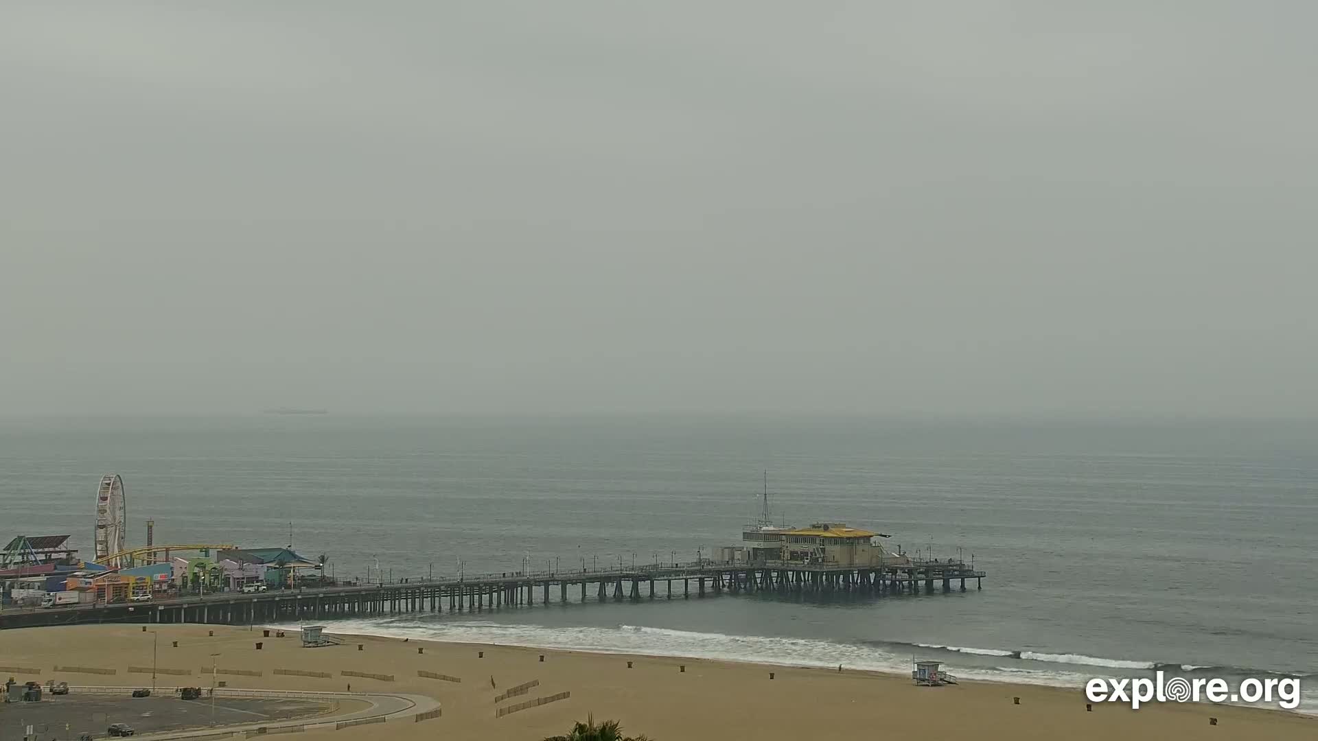 A long pier extends from a beach into a hazy, gray ocean.