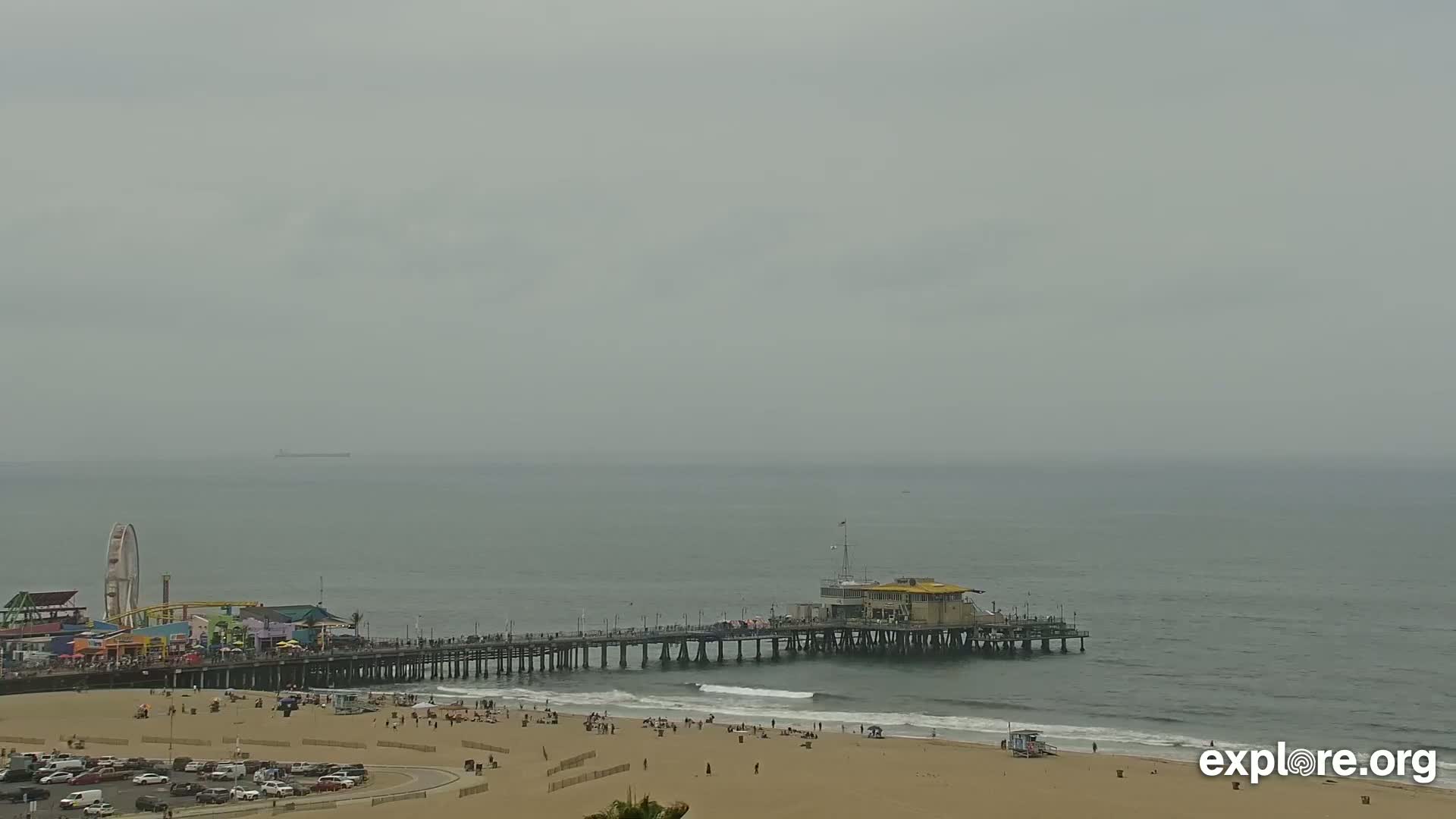 A long pier extends from a sandy beach into a calm, gray ocean under an overcast sky.