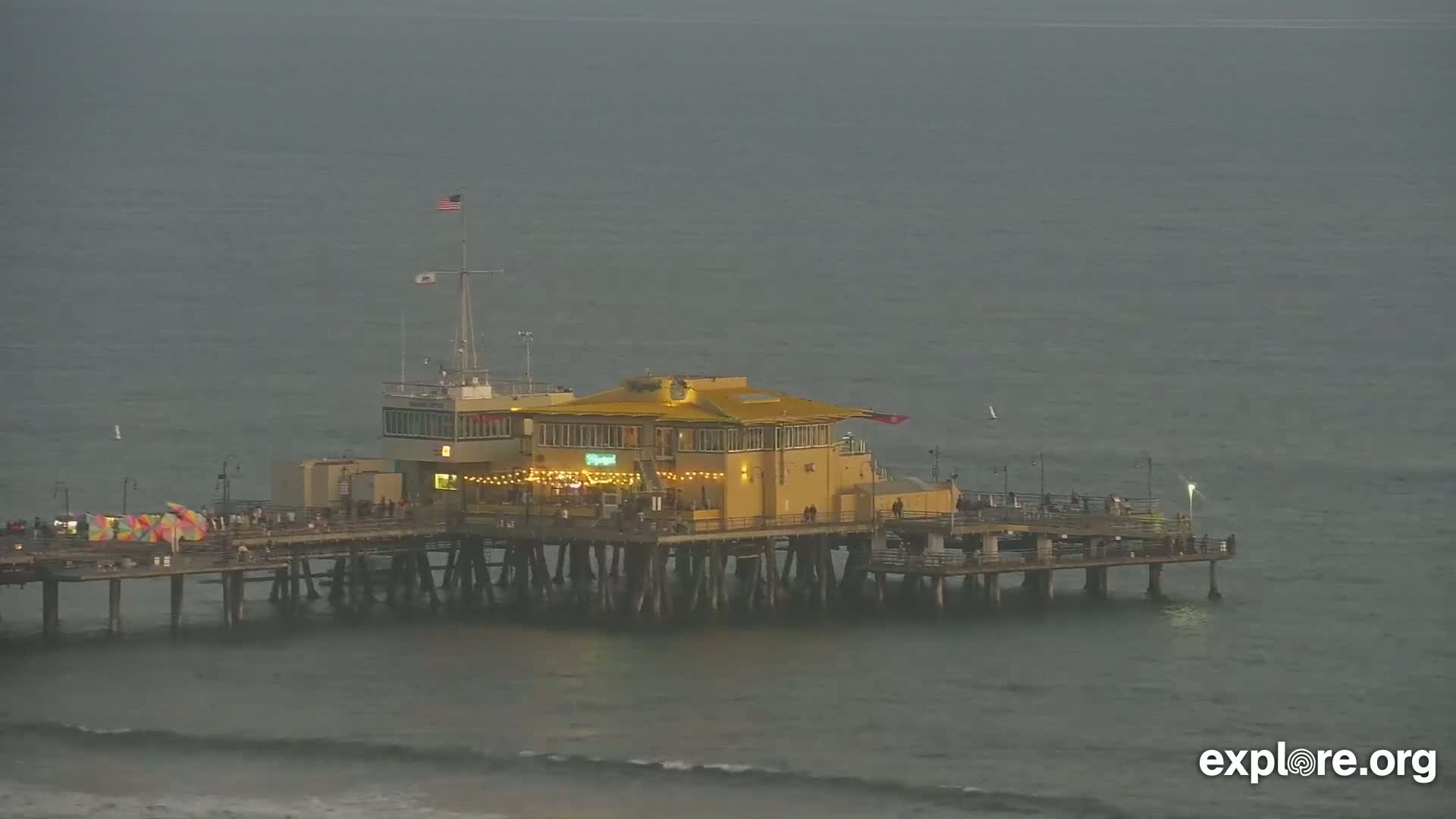 A pier with a building on it extends into a calm, gray-green ocean under an overcast sky.
