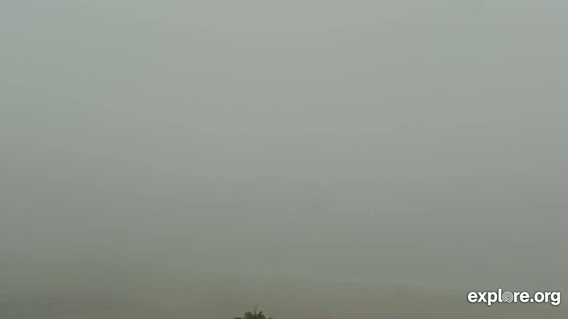 A hazy, overcast sky blankets a flat landscape with only a hint of vegetation visible at the bottom.