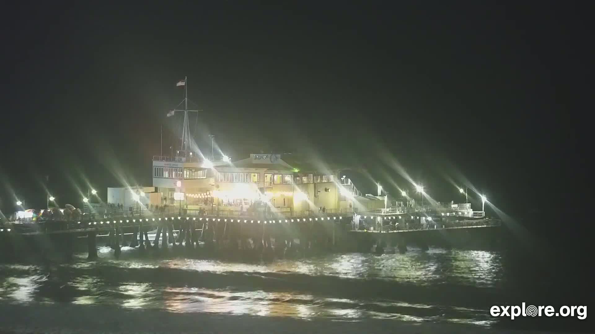 A brightly lit pier extends into a dark, choppy ocean at night.