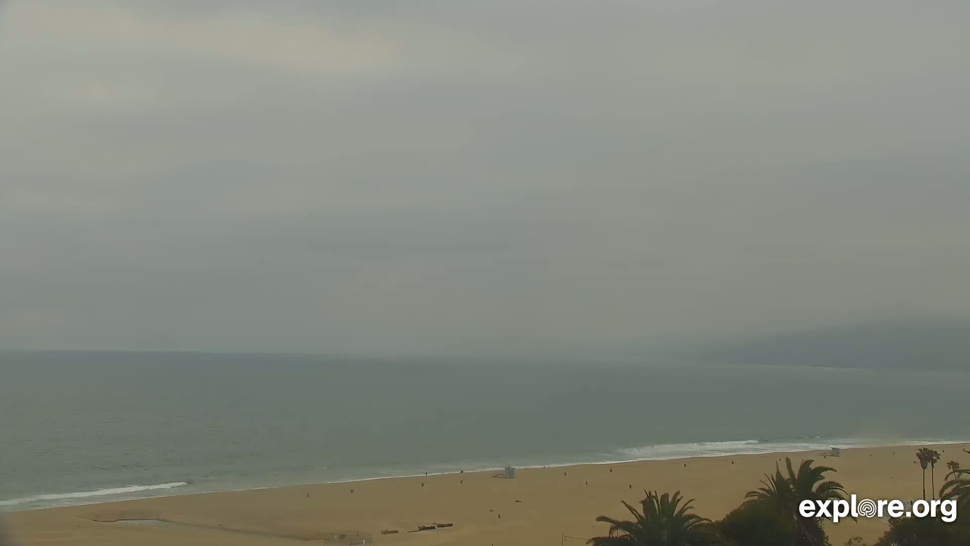 A mostly overcast sky hangs over a sandy beach and calm ocean.