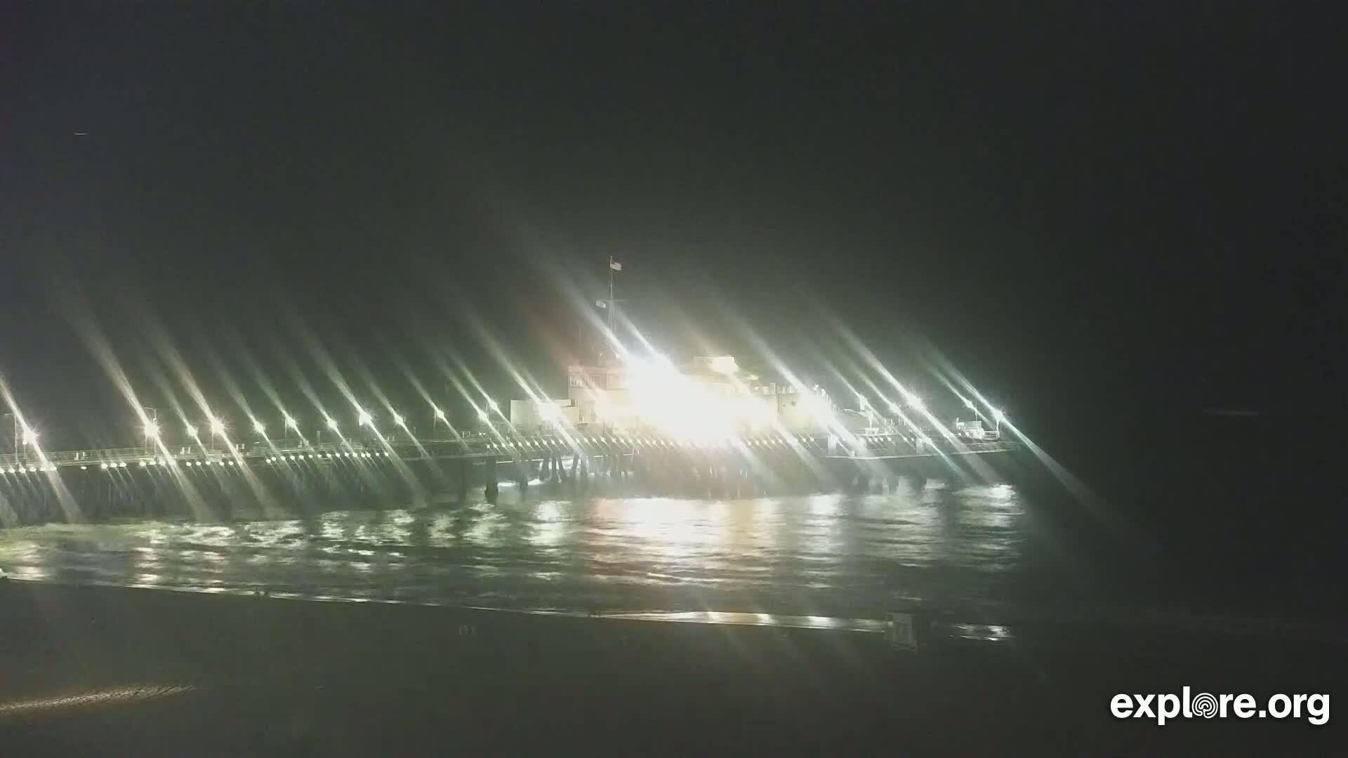 A brightly lit pier extends over dark, gently waving water at night.