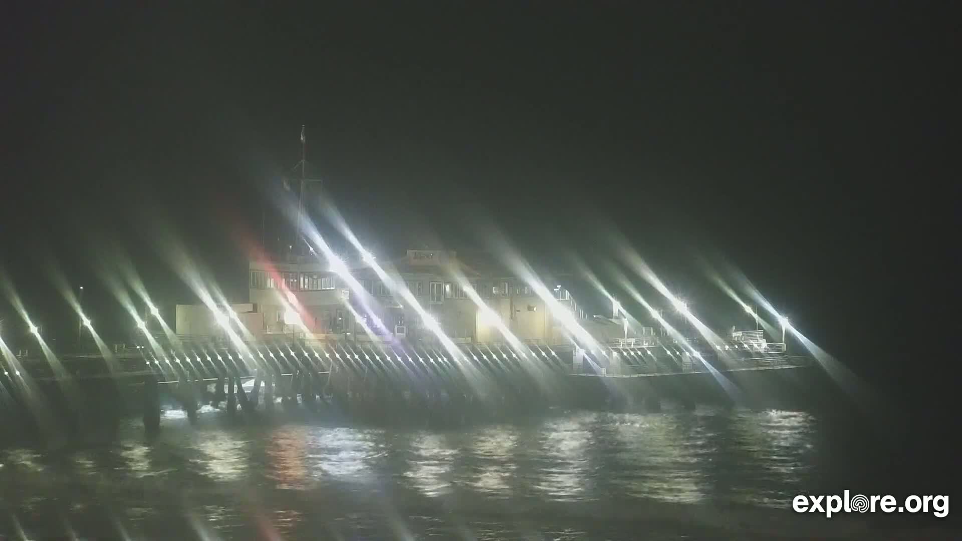 A brightly lit pier extends over dark, choppy water at night.