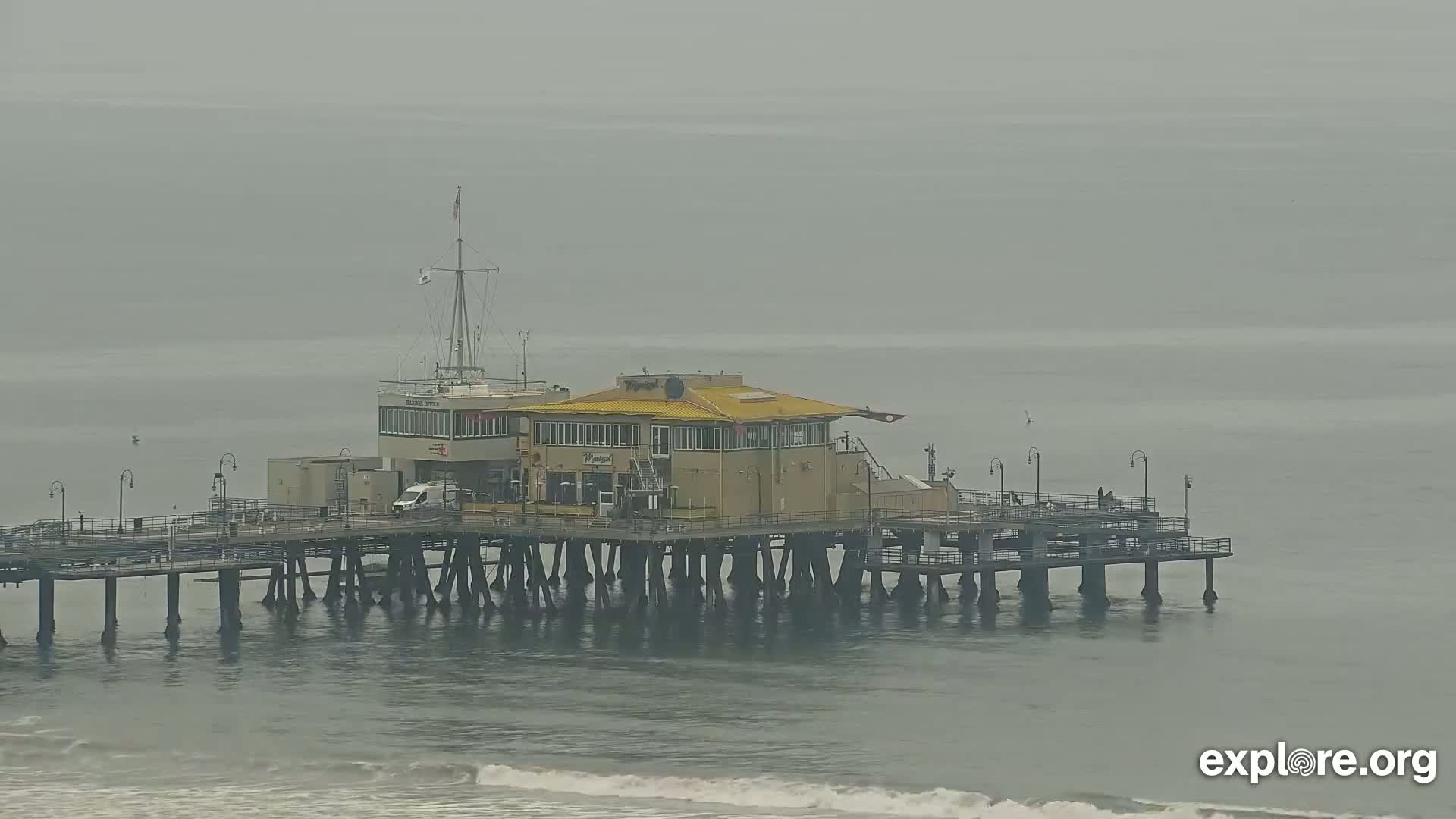 A pier with a building on it extends into a foggy ocean with small waves.