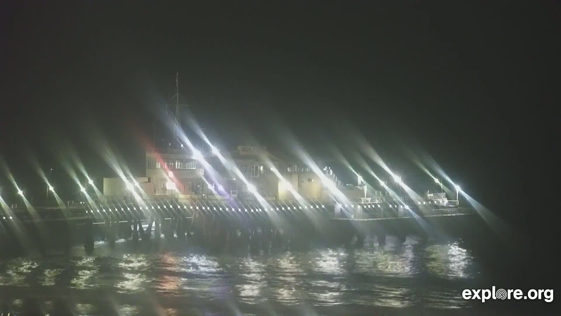 A brightly lit pier extends over dark, choppy water at night.
