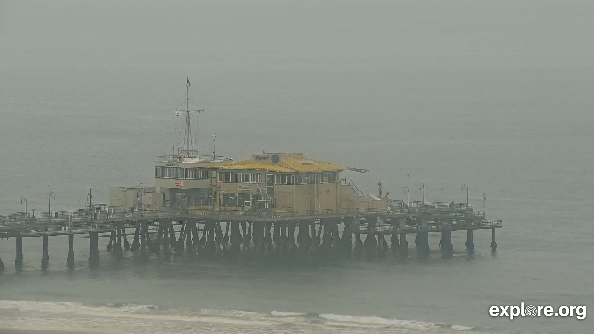 A long pier with a building on it extends into a foggy ocean.