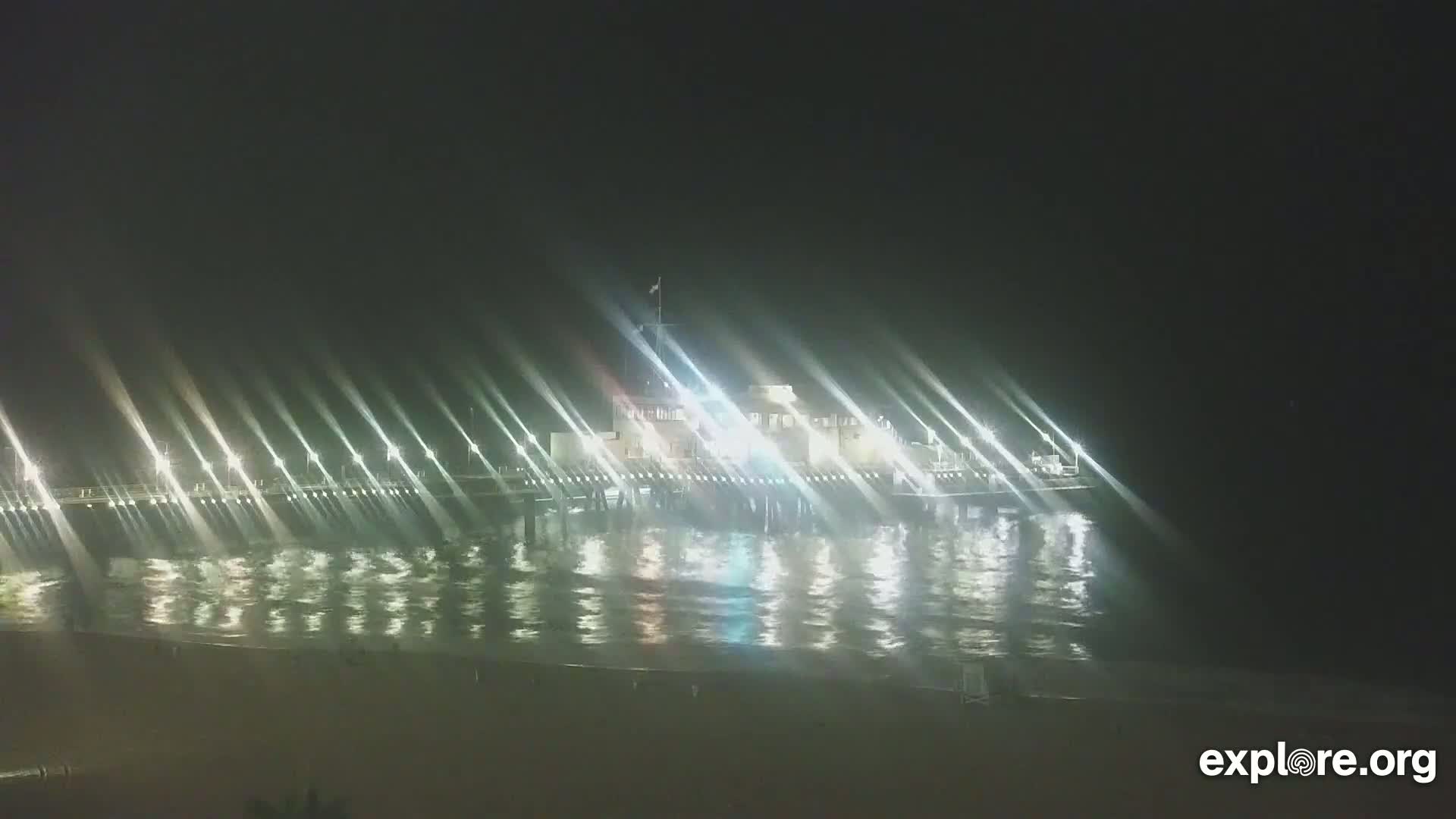 A brightly lit pier extends over dark, gently rippling water at night.
