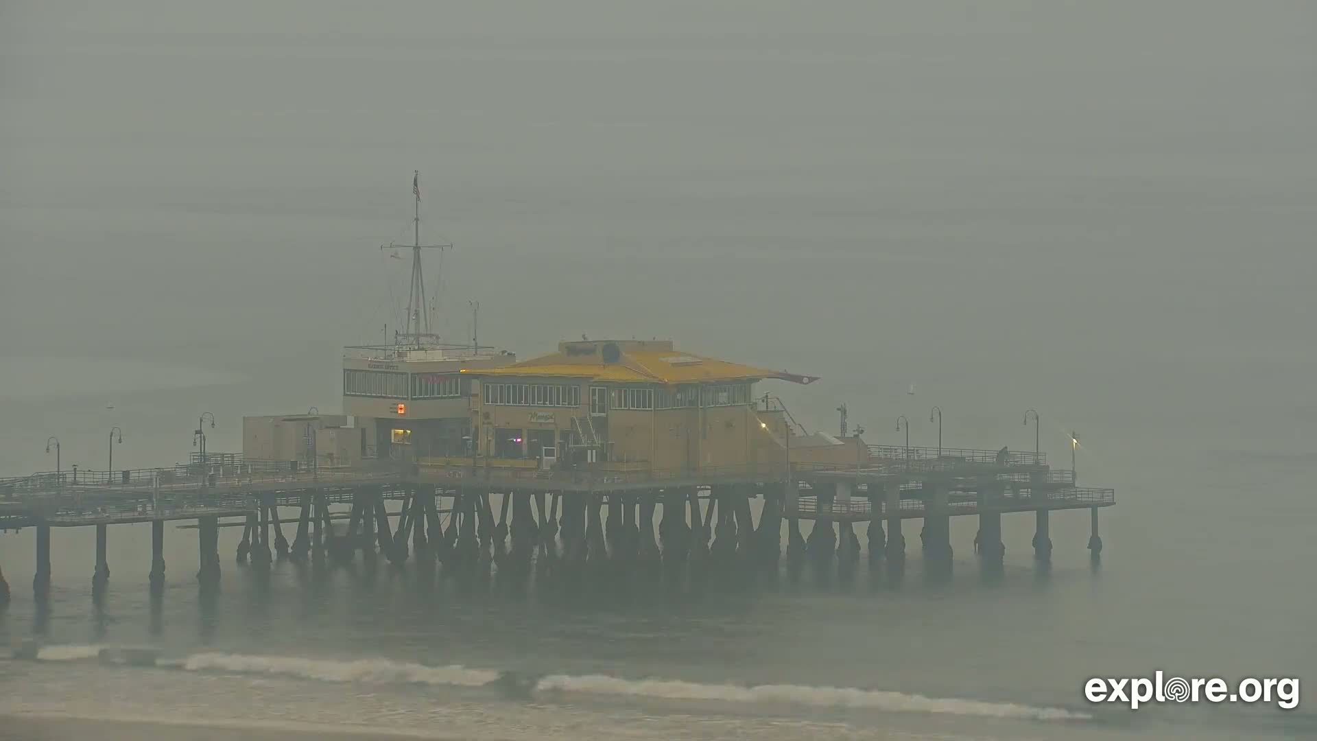 A pier with a building on it sits on the ocean, obscured by heavy fog.