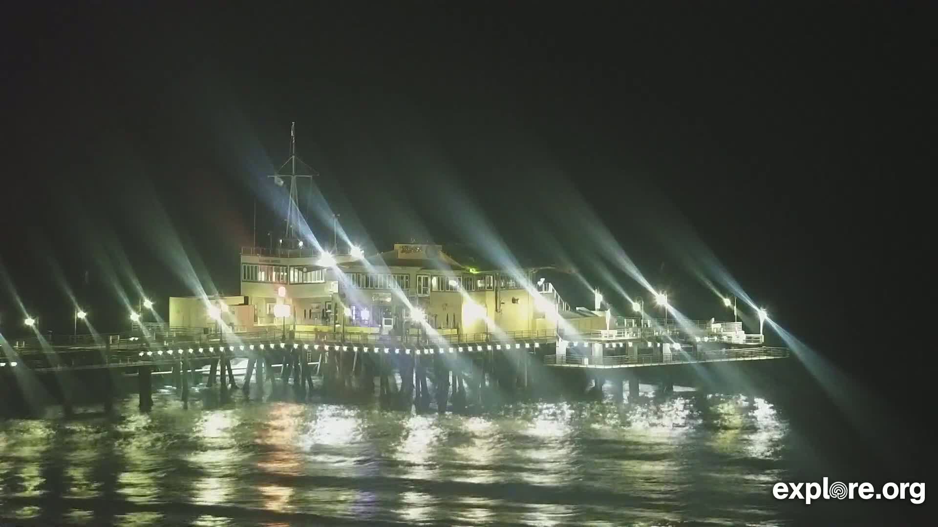 A brightly lit pier stands over dark, gently waving water at night.
