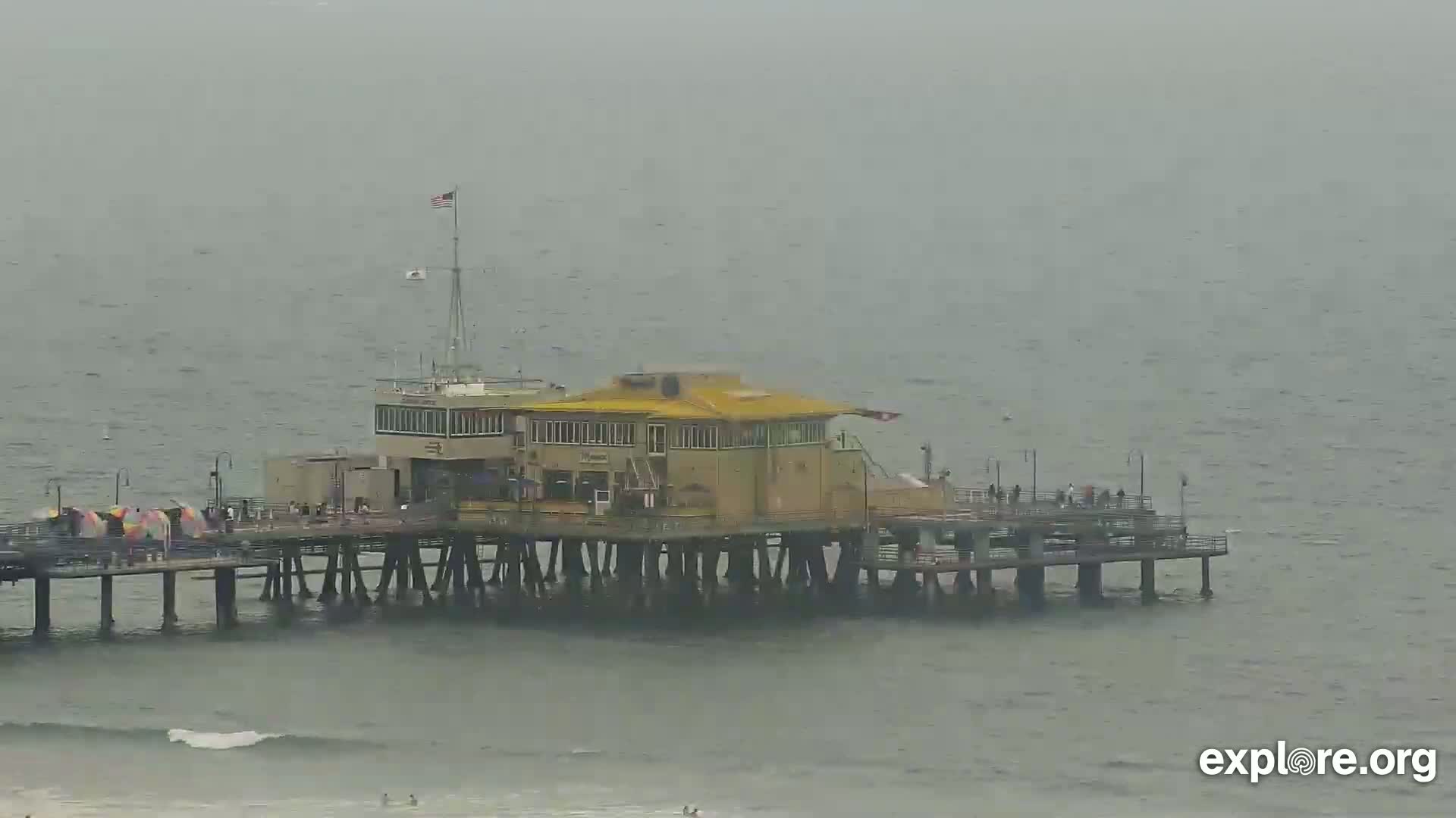 A pier with a building on it extends into a gray, overcast ocean.
