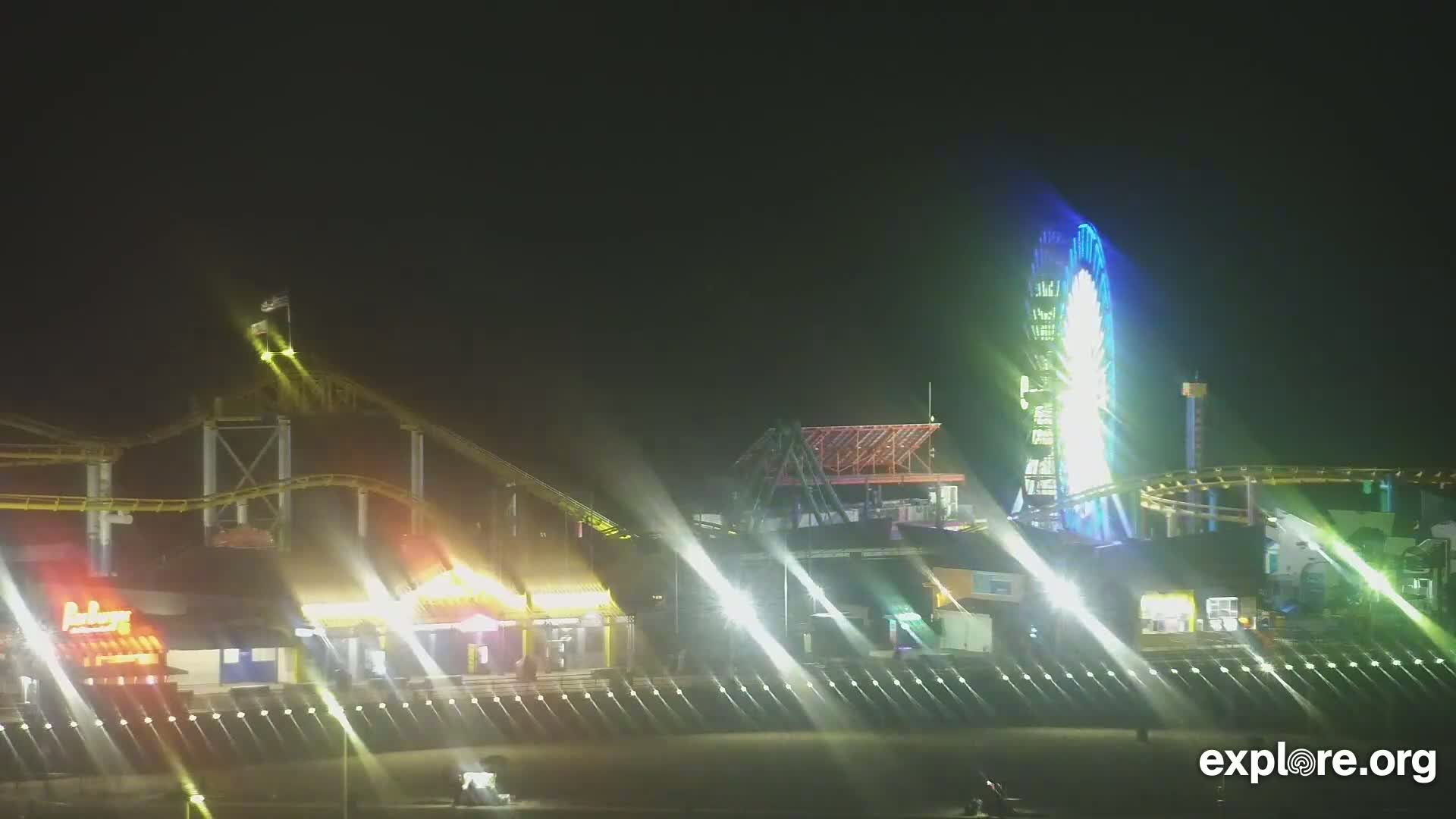 A brightly lit nighttime amusement park with a Ferris wheel and roller coasters is visible under a dark sky.