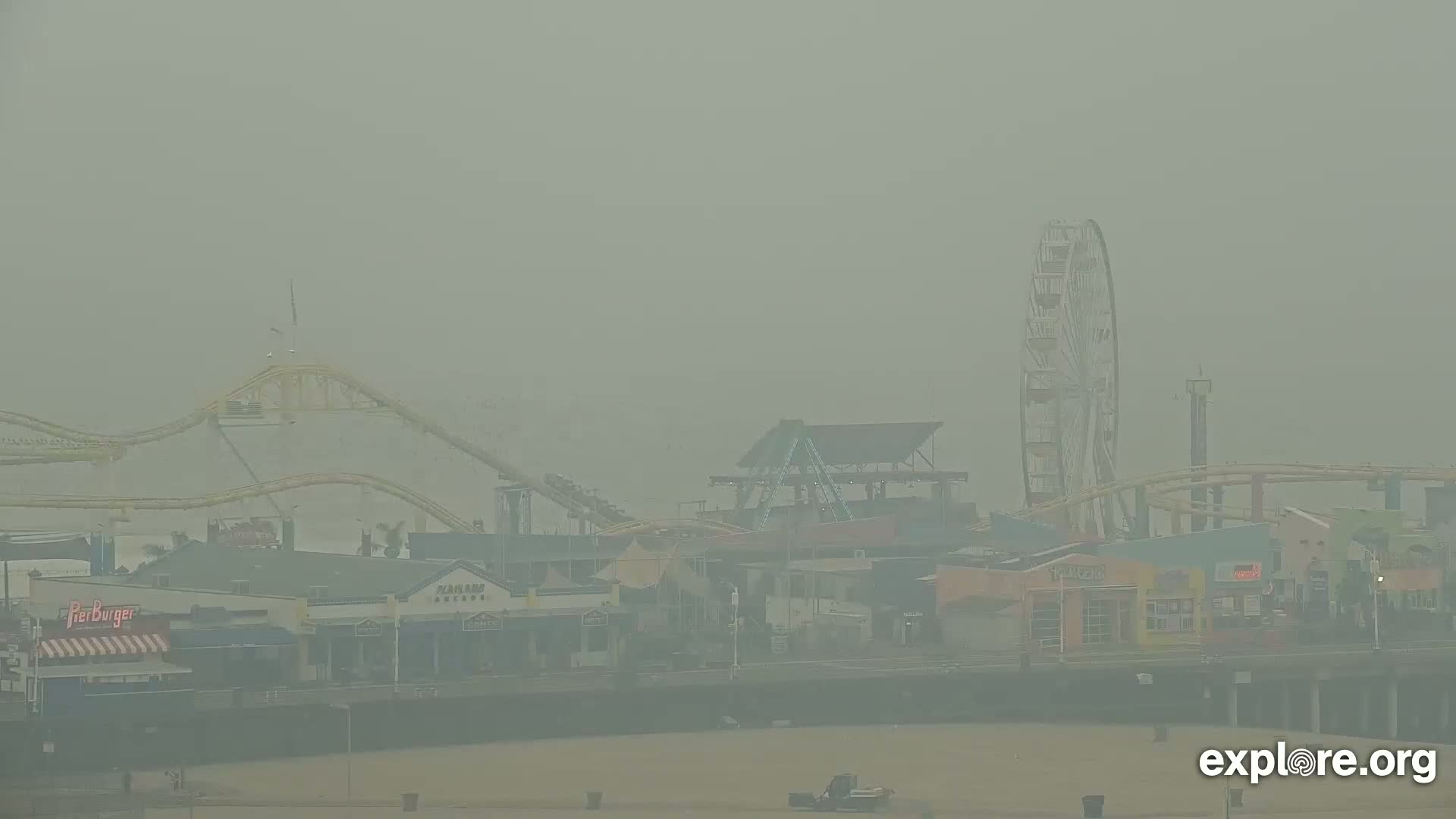 A hazy view of a pier with a Ferris wheel, roller coaster, and various buildings.