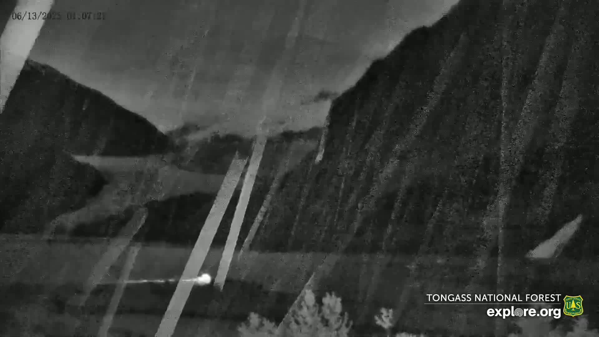 A nighttime, rainy view shows dark mountains and a small light source in the lower center.