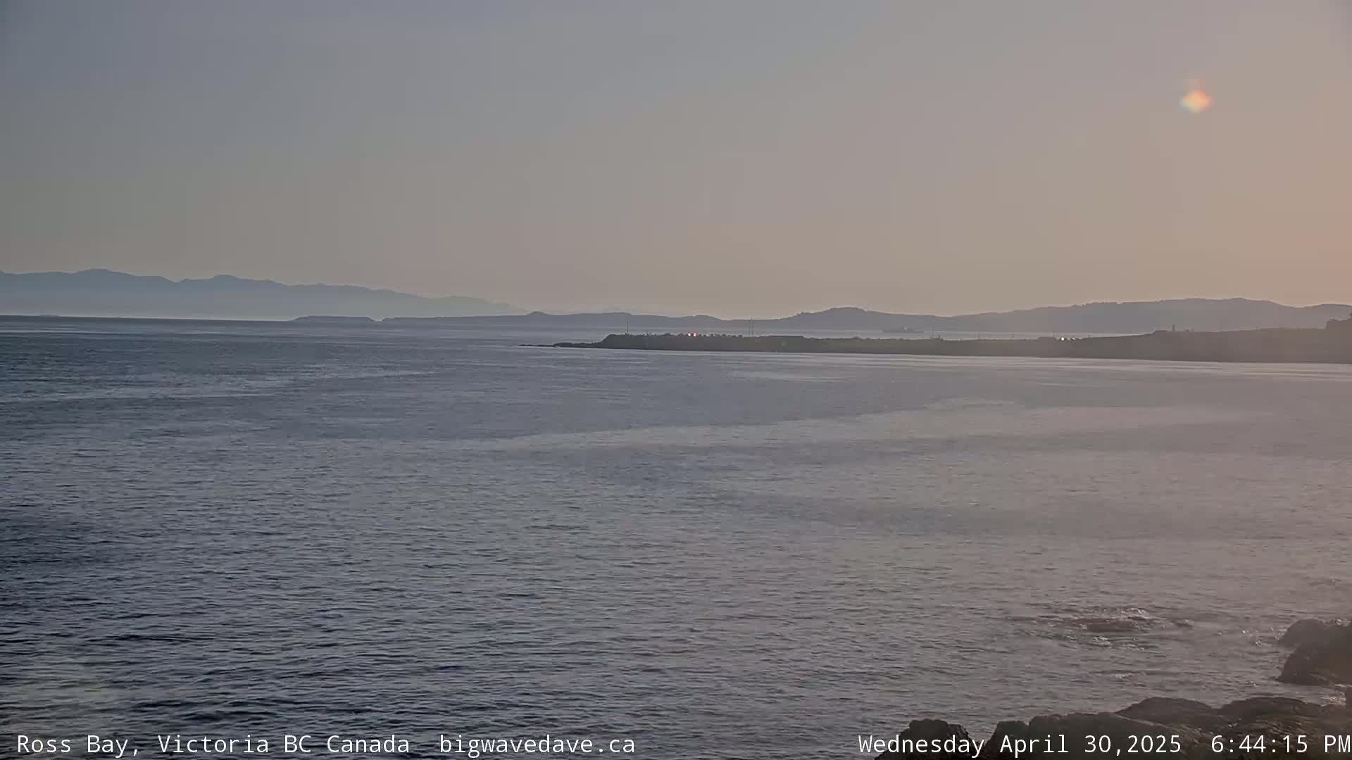 A calm ocean bay with a distant mountain range under a hazy sky.