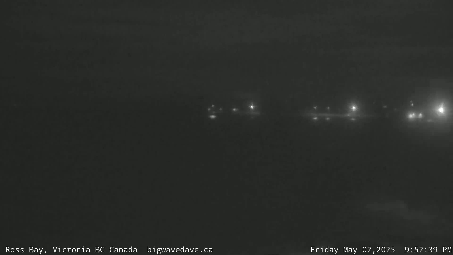 A dark, nighttime scene shows a faint line of distant lights across a hazy or foggy body of water.