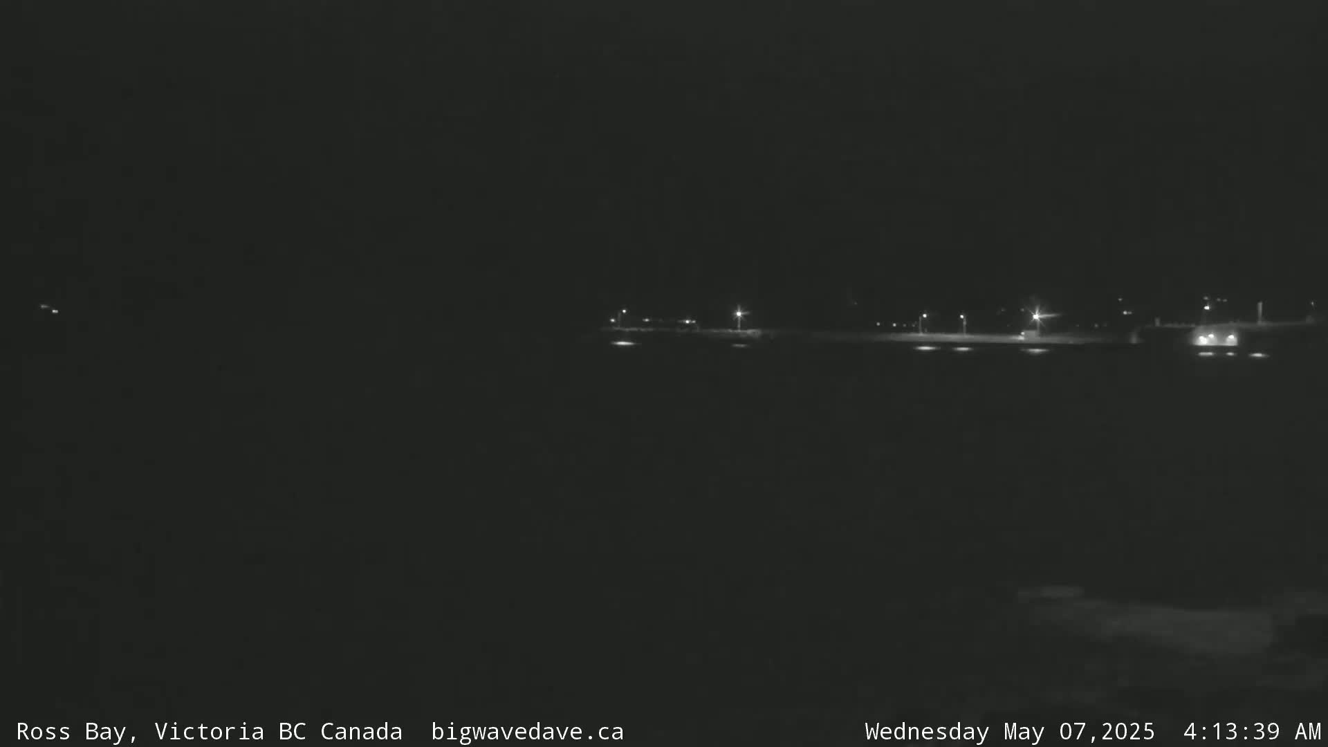 A nighttime, low-light view of a dark, flat landscape with a few distant lights visible.