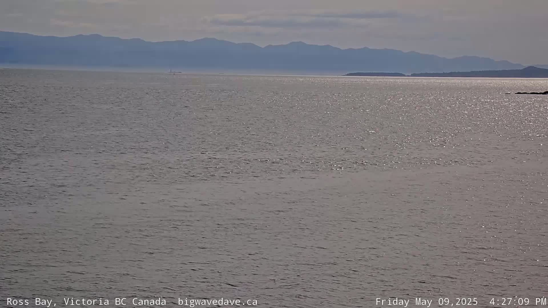 A calm body of water stretches to a distant mountain range under a mostly clear sky.