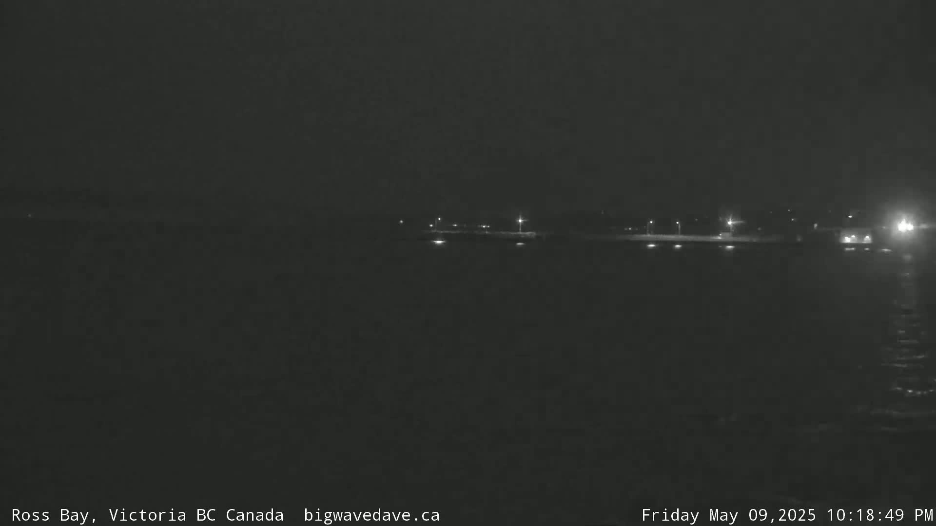 A nighttime, dark view of a body of water with dimly lit structures visible in the distance.