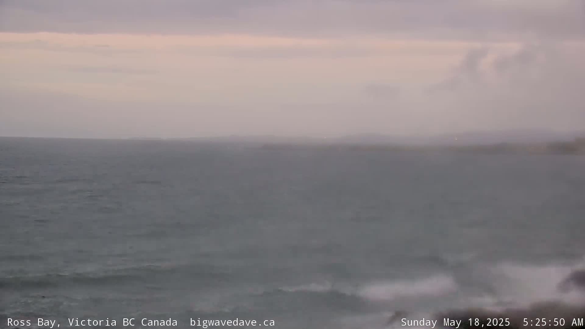 A mostly overcast sky hangs over a gray ocean with small waves breaking near the shore.