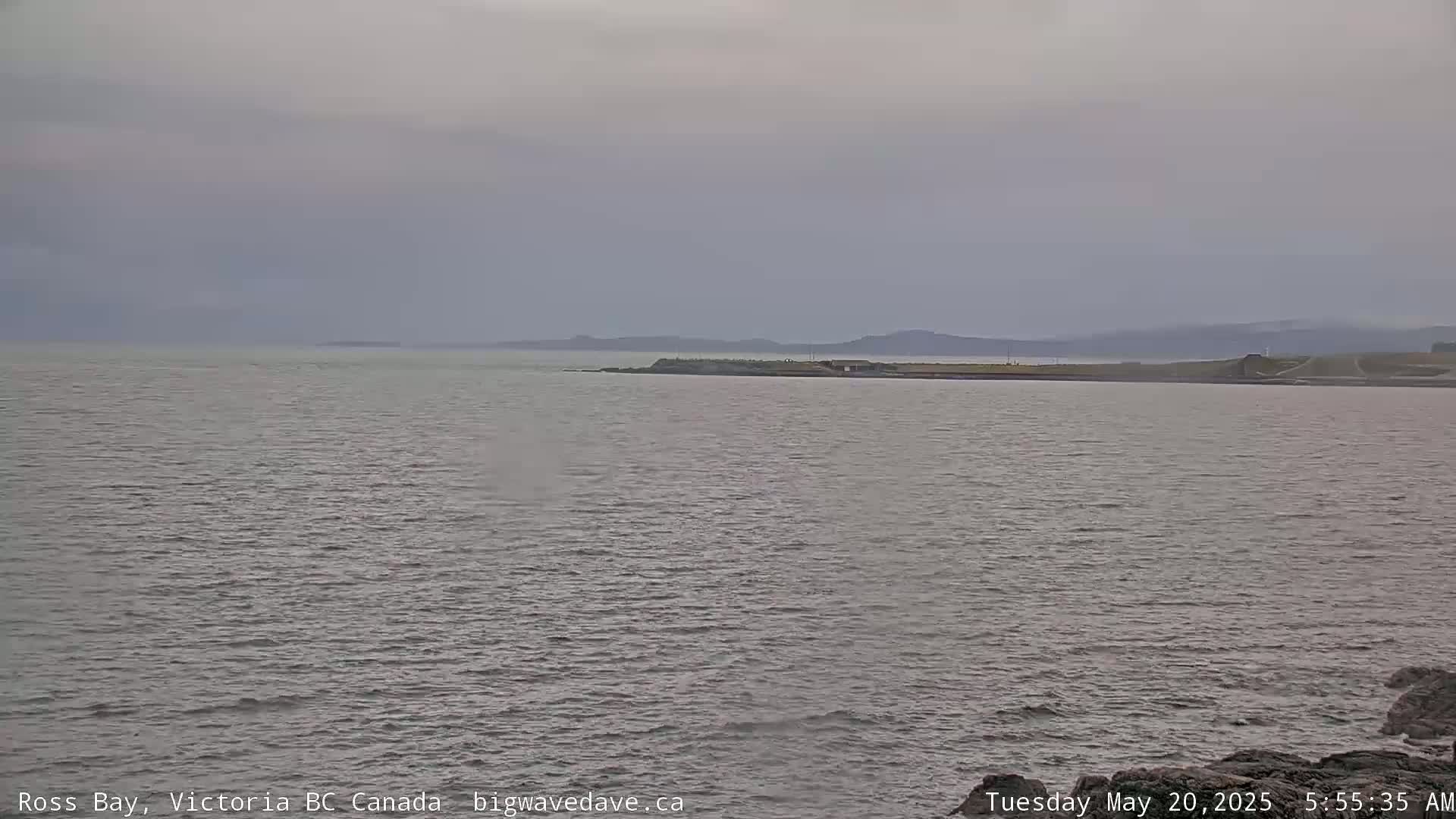 A calm, overcast day reveals a wide expanse of gray water with a distant shoreline under a muted sky.