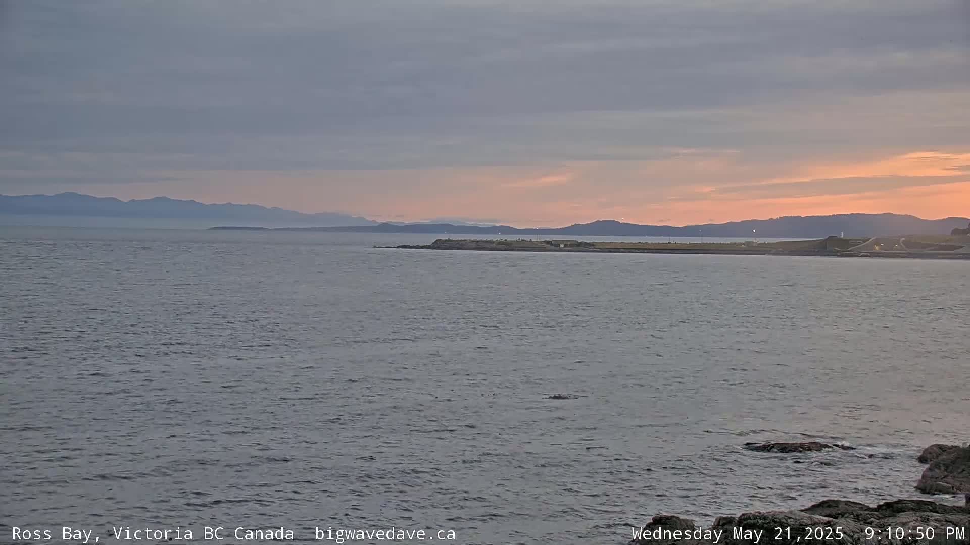 A calm ocean with a distant mountain range under a dusky pink and gray sunset sky.