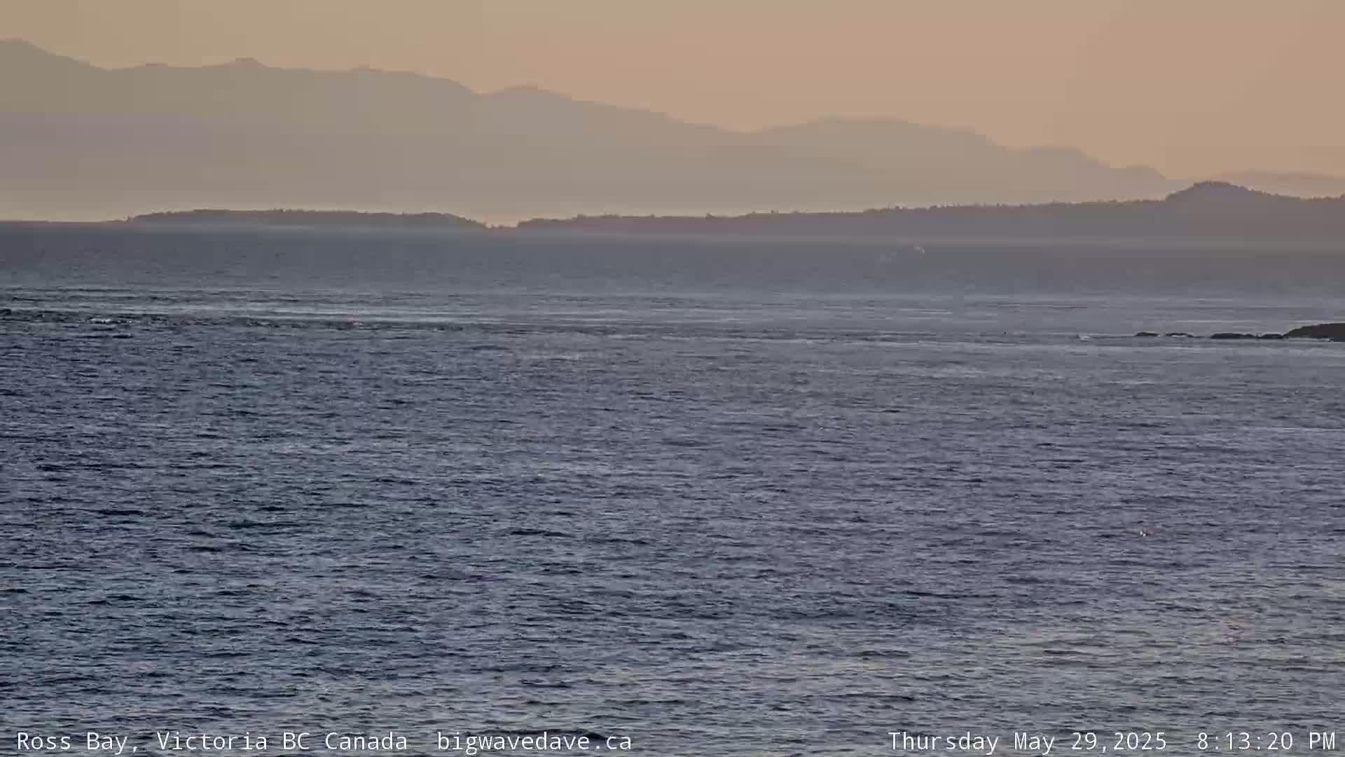 A calm ocean with a distant, hazy mountain range under a pale sunset sky.