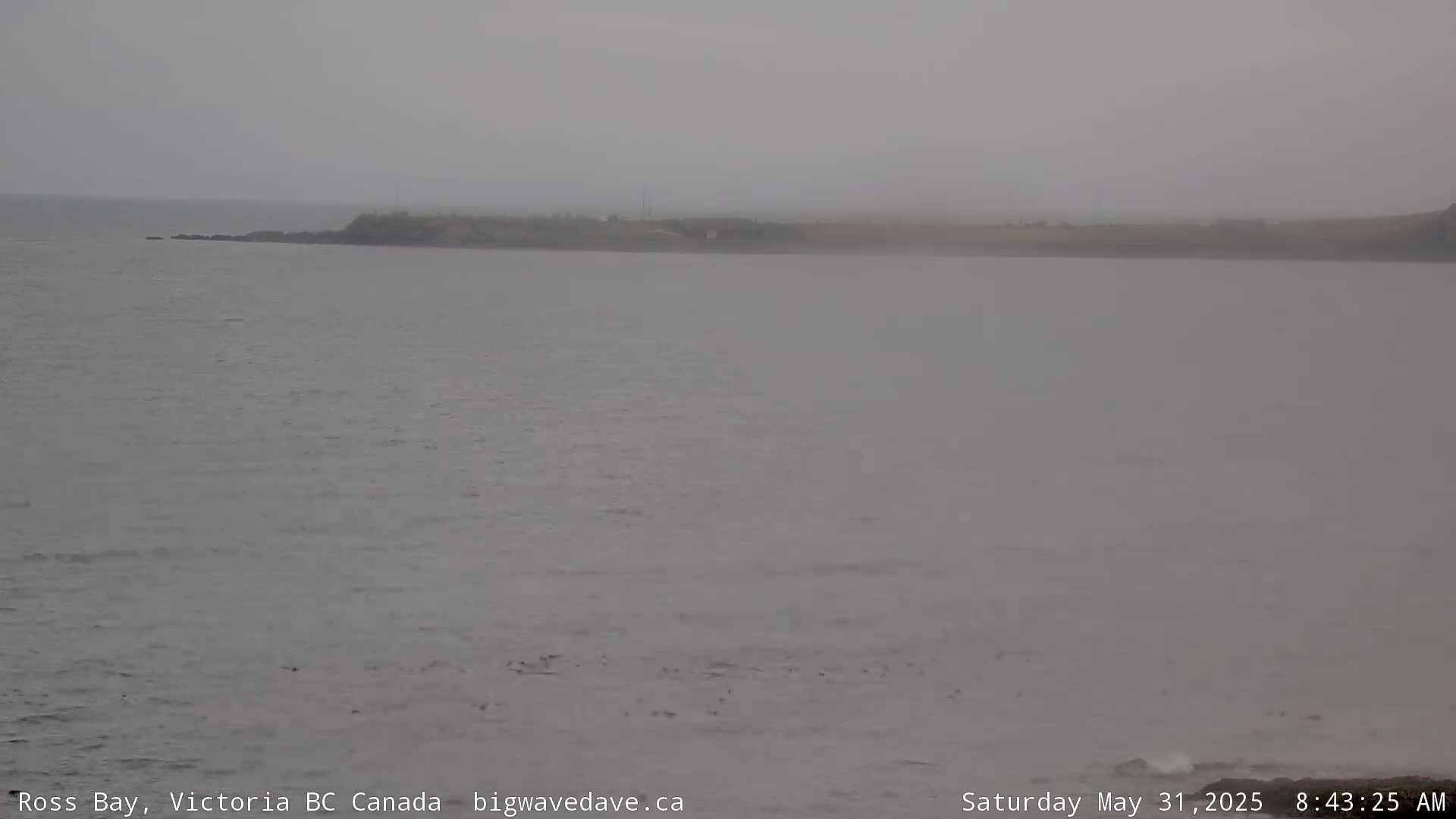 A hazy, overcast day reveals a calm body of water with a distant, low-lying shoreline.