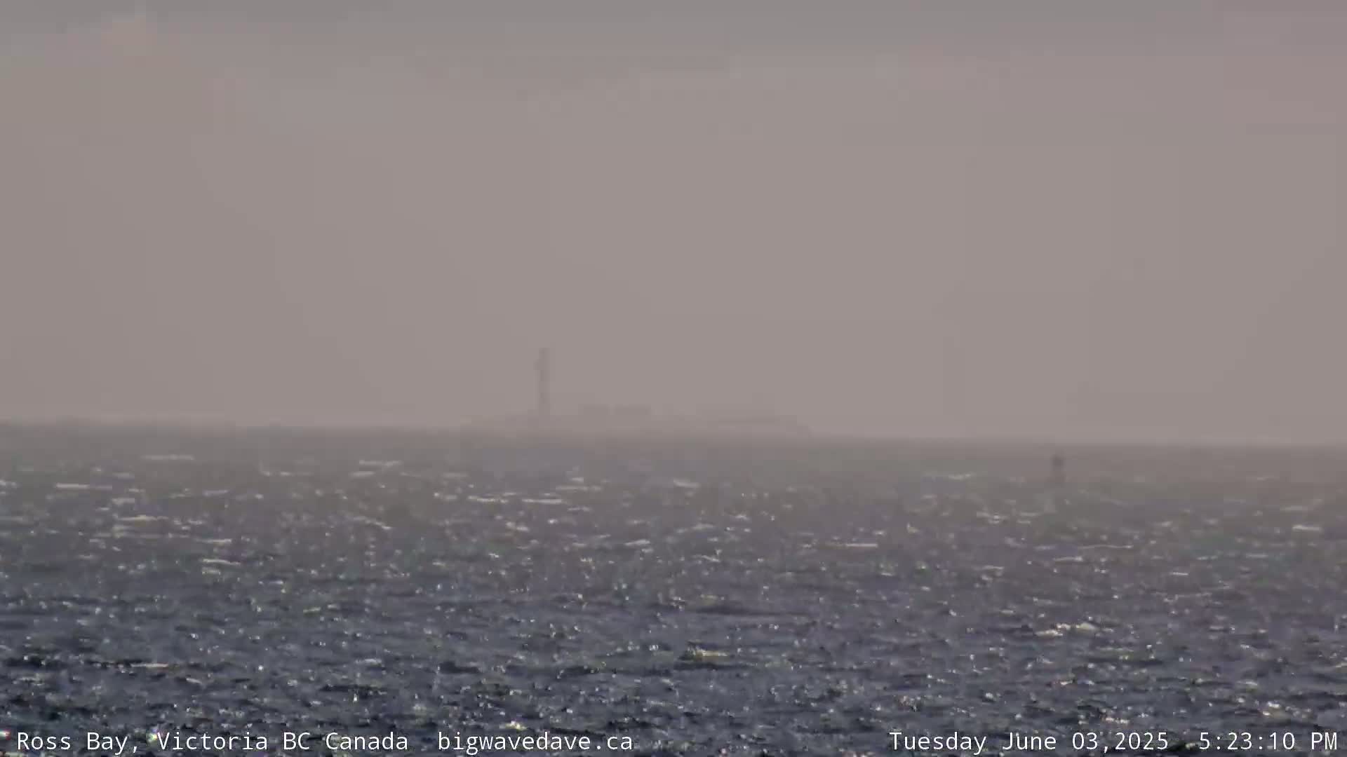 A hazy, windy day shows a choppy ocean with a distant lighthouse barely visible.